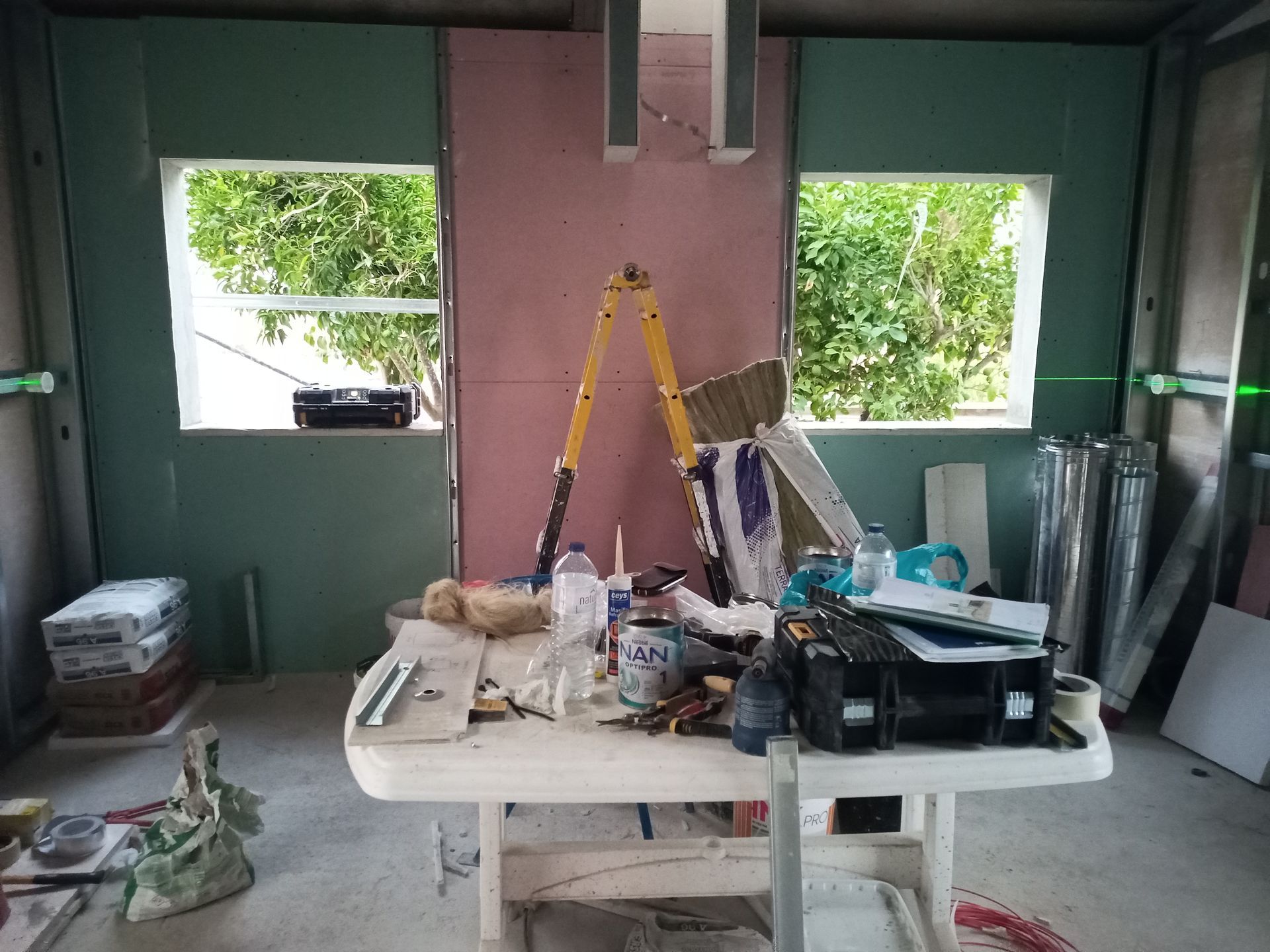 Interior de um cômodo em construção, com janelas e materiais de construção sobre uma mesa.