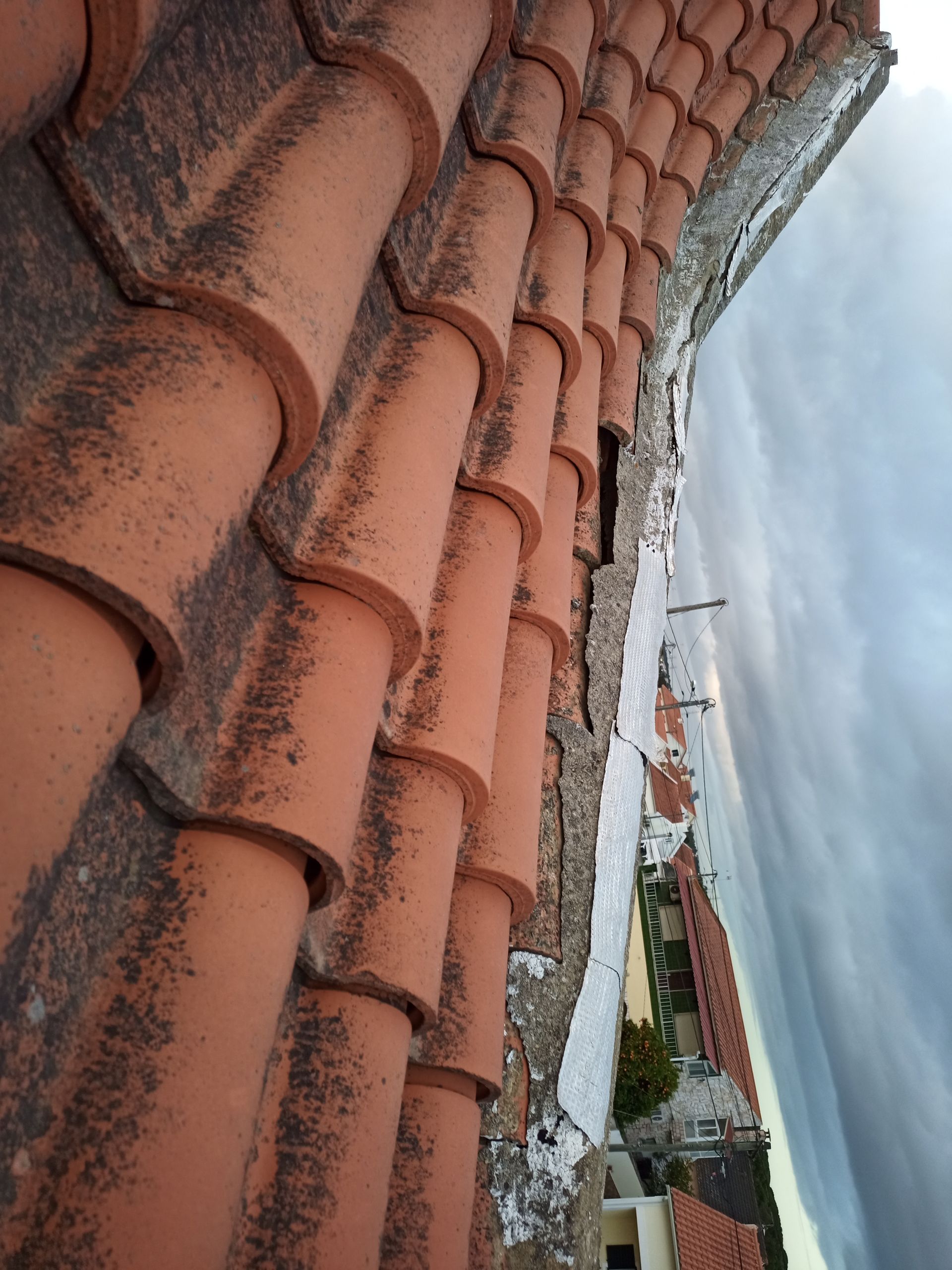 Borda do telhado de telha laranja com vista para os edifícios e o céu.