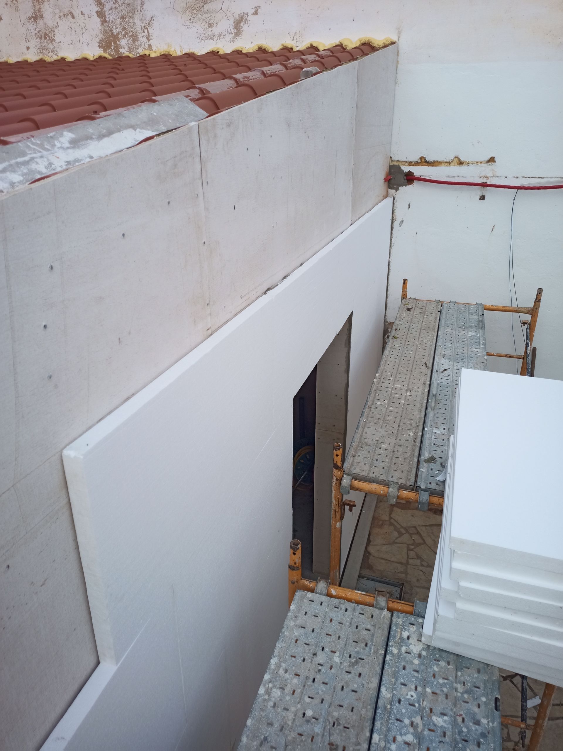 Parede externa com painéis isolantes brancos sendo instalados, ao lado do andaime.