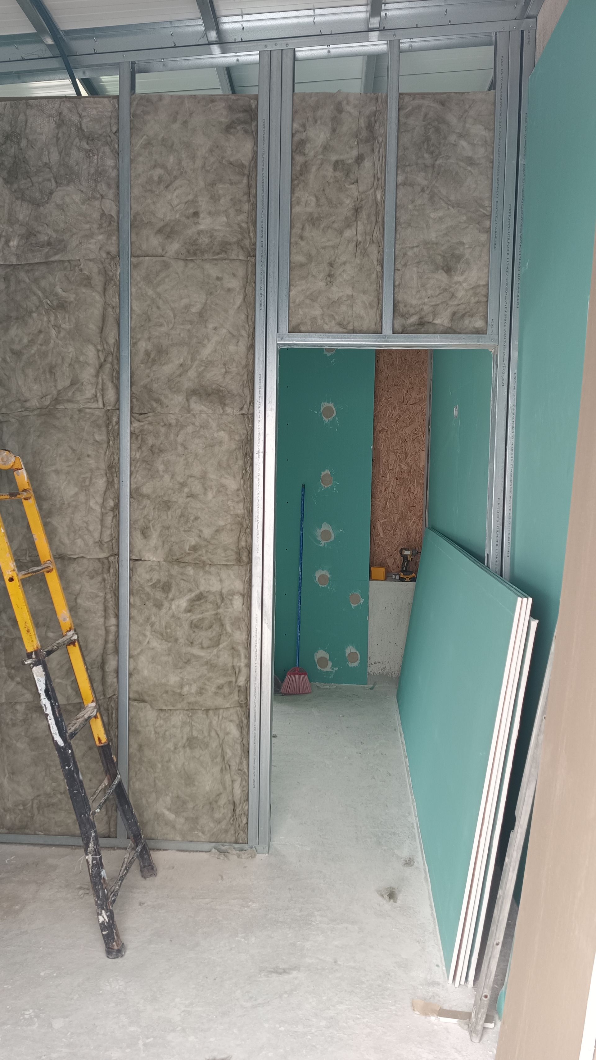 Construção interna de uma porta, estrutura metálica, isolamento e drywall. Uma escada está encostada na parede.