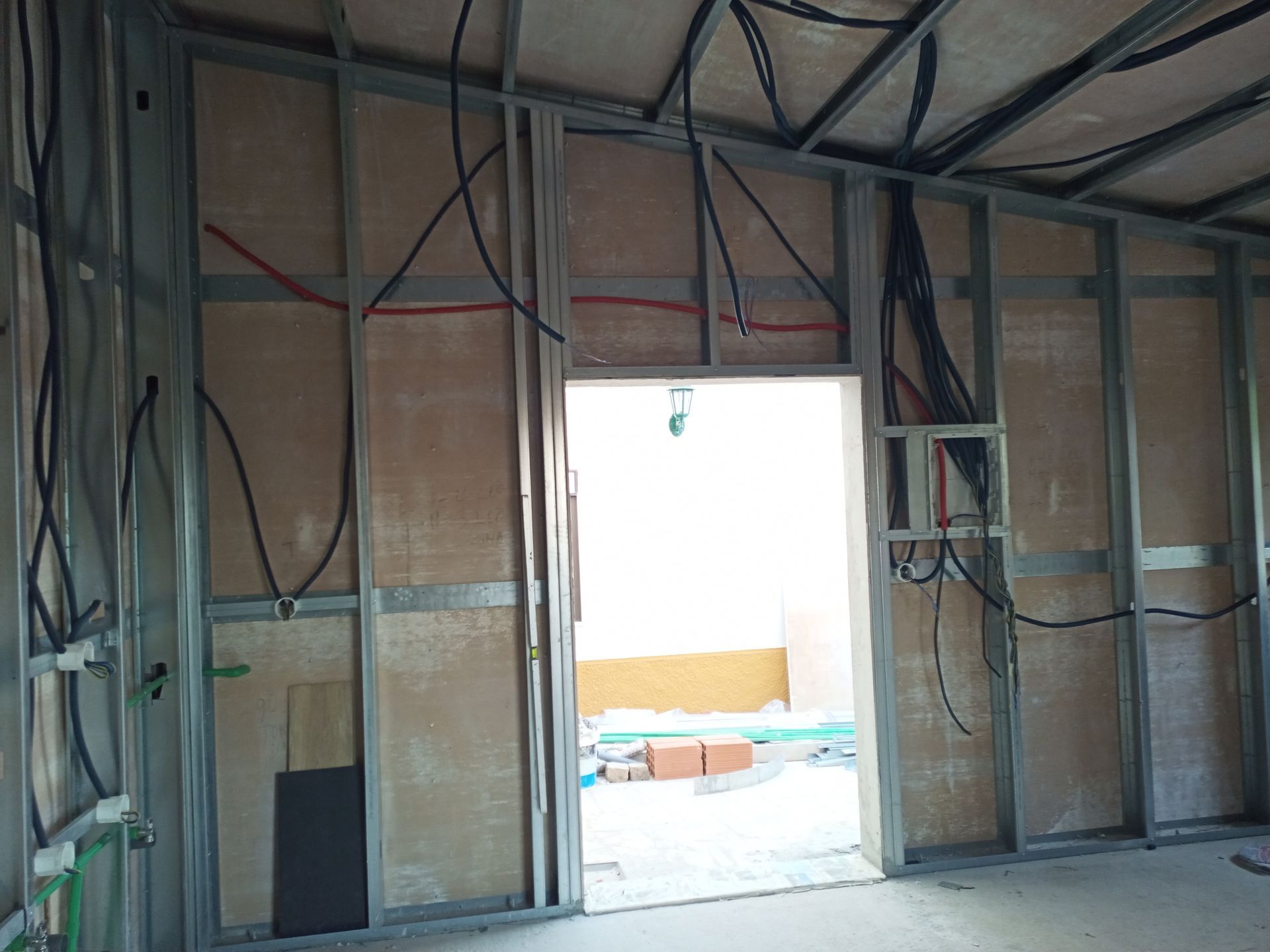 Vista interna de um cômodo em construção, mostrando a estrutura metálica, a fiação exposta e a porta que dá acesso a outro cômodo.