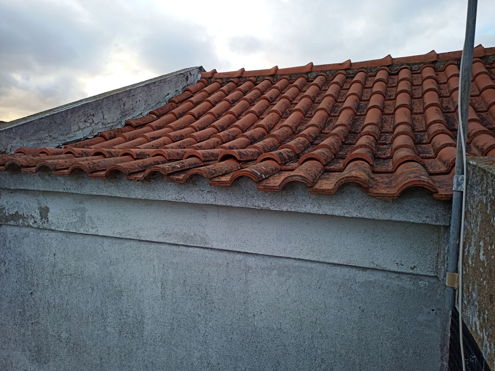 Telhado de telha vermelha em um prédio de concreto contra um céu nublado.