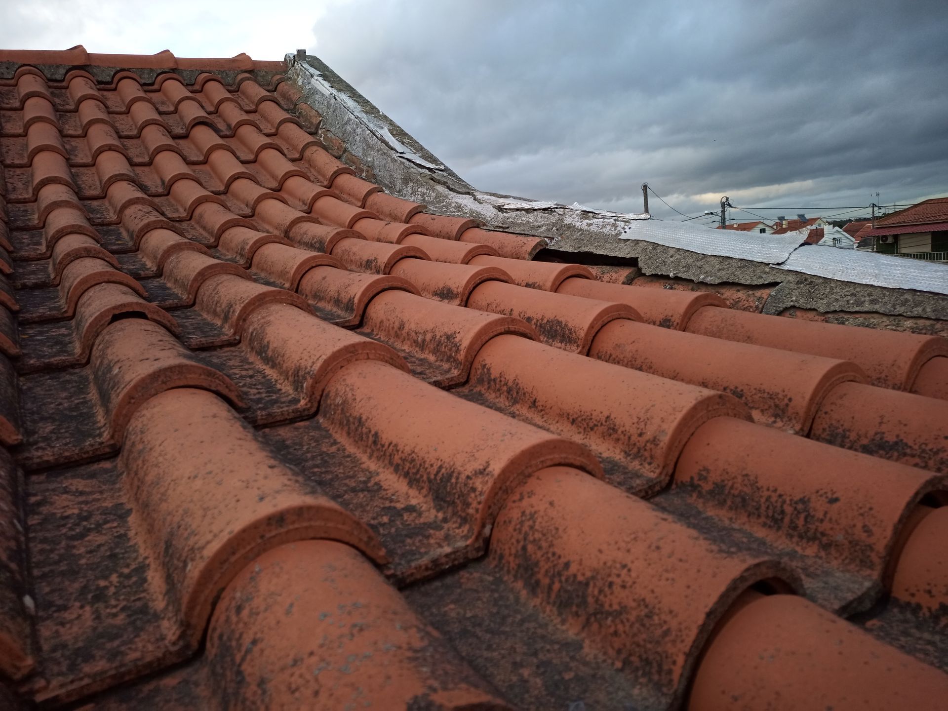 Telhado de telhas de barro vermelho com manchas de neve sob um céu nublado.