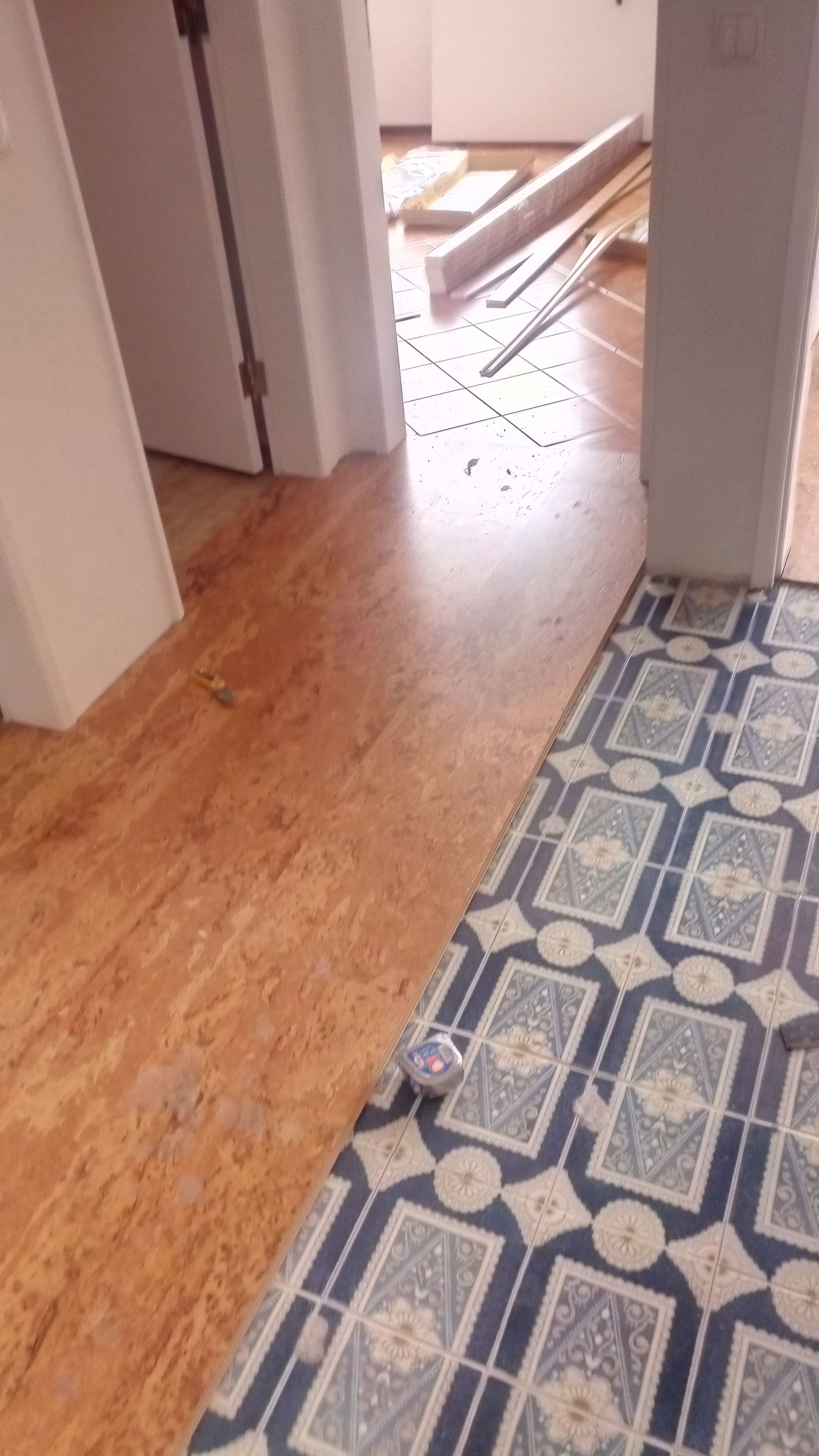 O piso de madeira dá lugar a um piso de ladrilhos estampados perto de uma porta, onde há um objeto prateado sobre os ladrilhos.