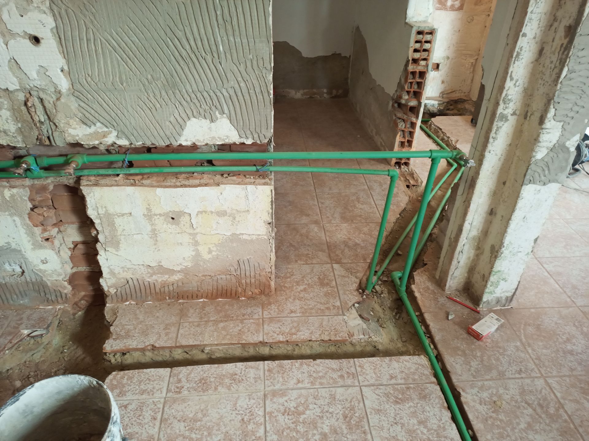 Reforma em andamento: tubulações verdes percorrem o piso de azulejos e paredes parcialmente expostas.