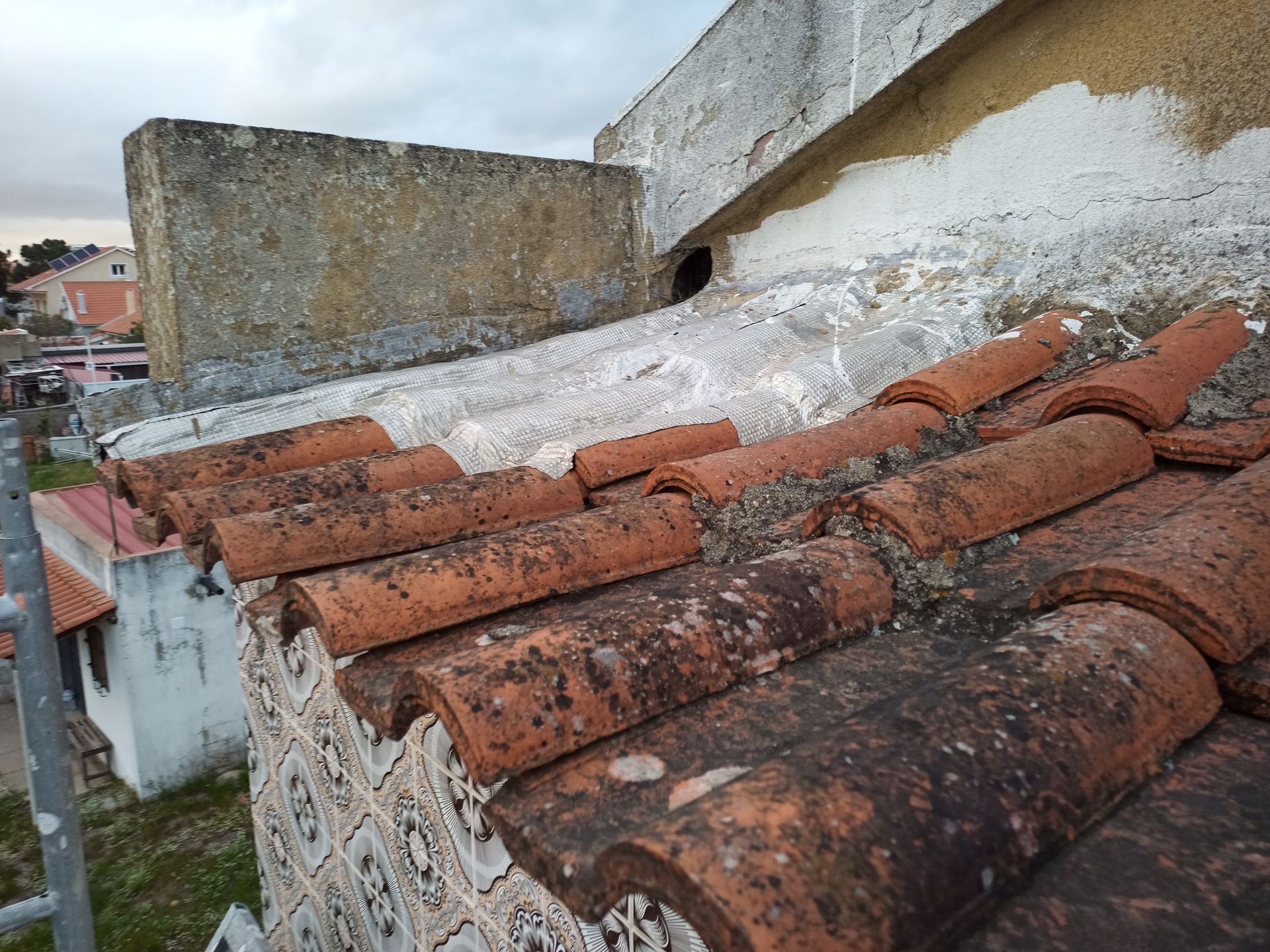 Um close-up de um telhado de telhas de barro desgastadas, com uma estrutura de blocos de cimento erguendo-se a partir dele.