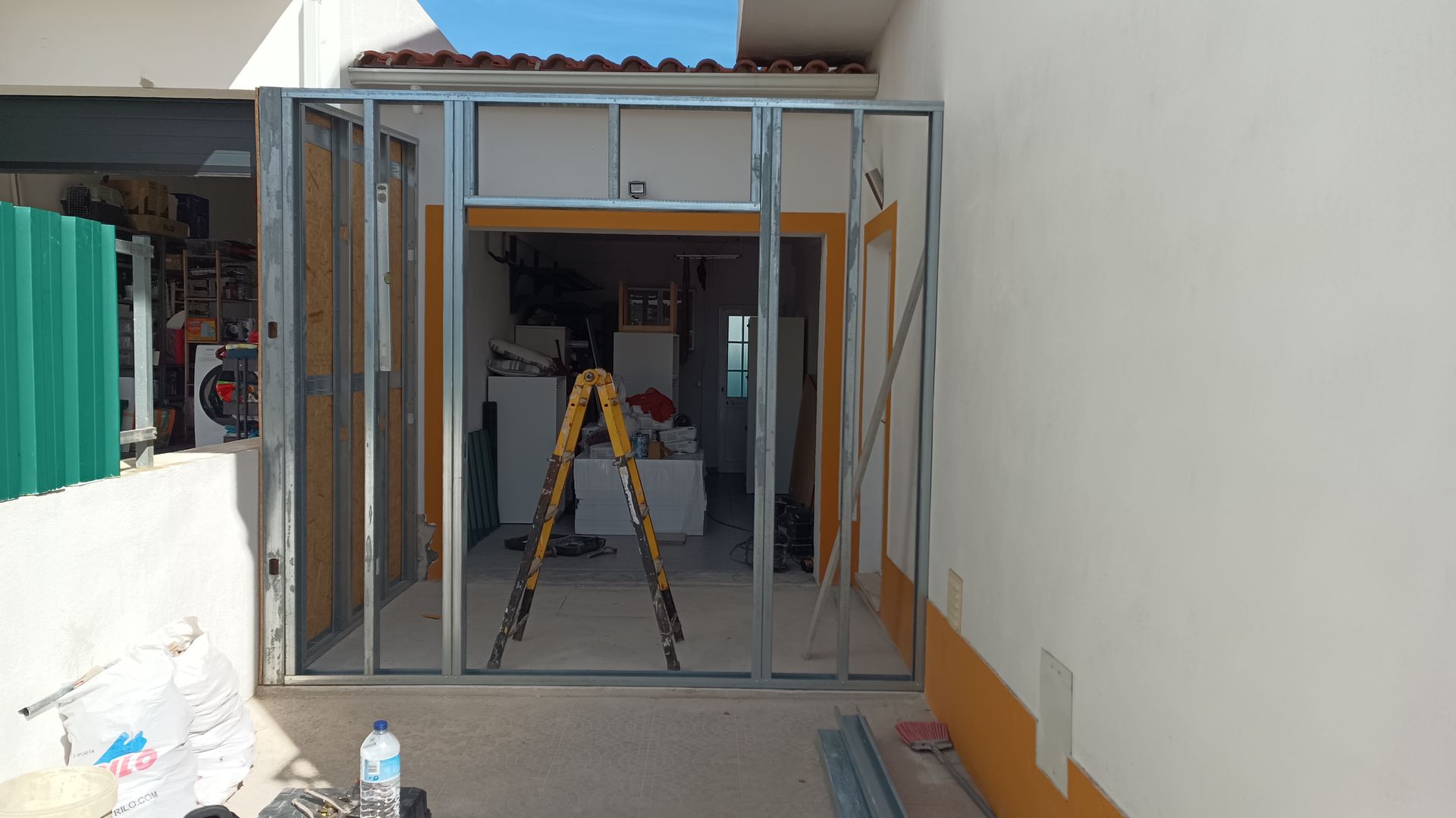 Estrutura metálica de uma porta com escada no interior, pronta para instalação de drywall, ao lado de uma parede amarela.