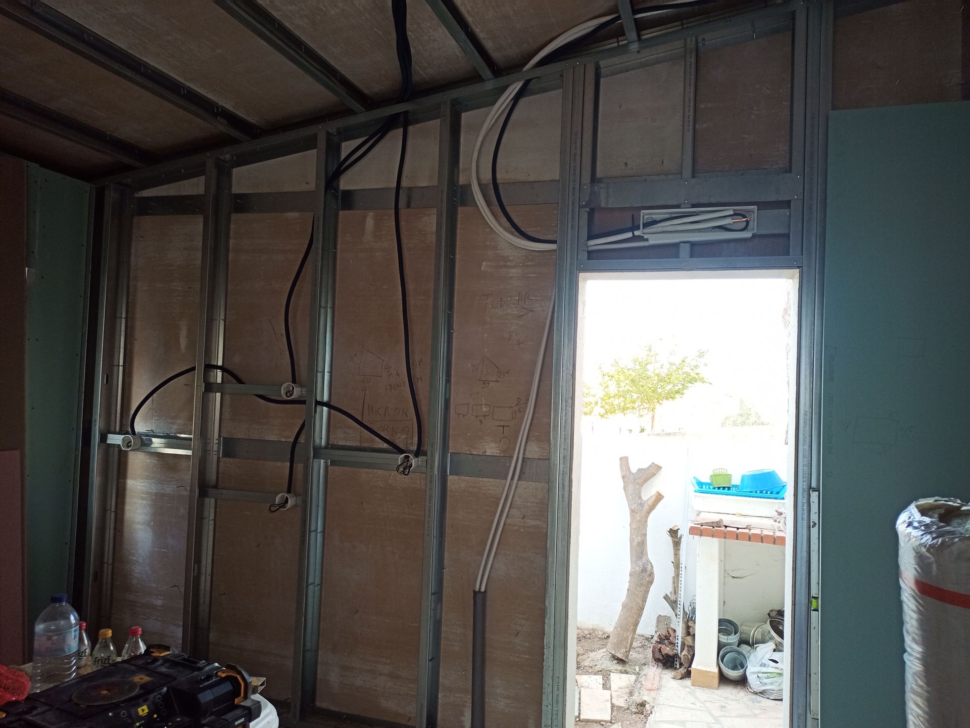 Estrutura da parede interna com fiação elétrica, porta e drywall sem acabamento.