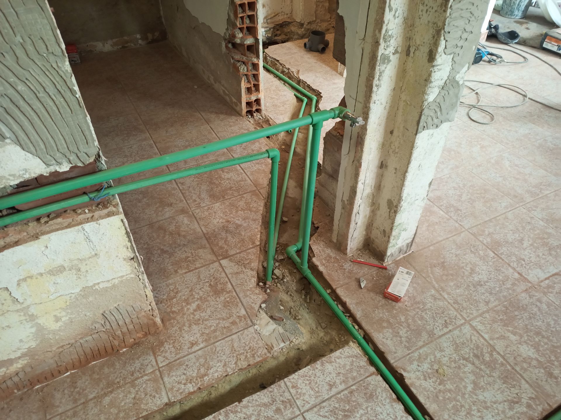 Tubulações de encanamento verdes atravessam um piso de azulejos em uma obra.