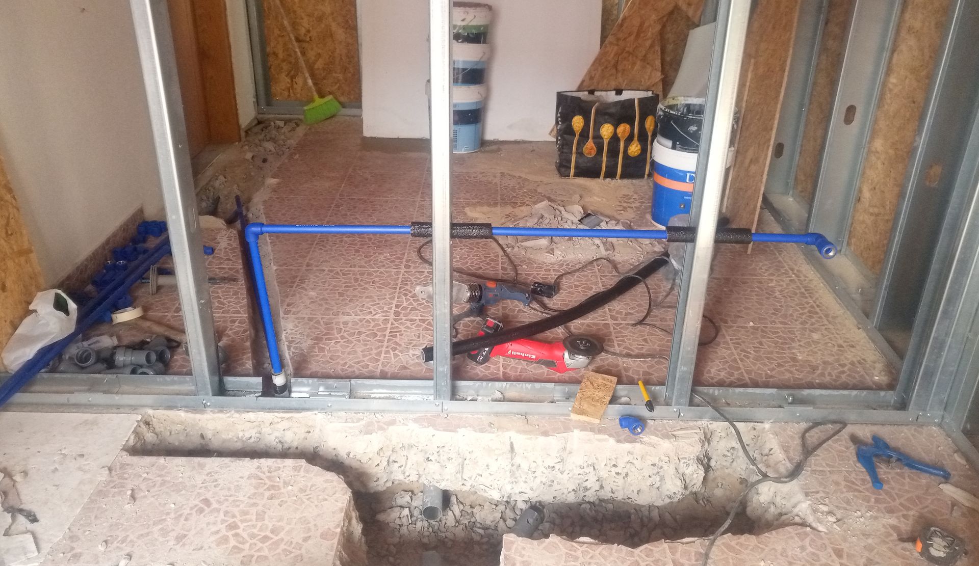 Construção interna: perfis metálicos, tubos azuis, isolamento exposto, esmerilhadeira, piso inacabado.