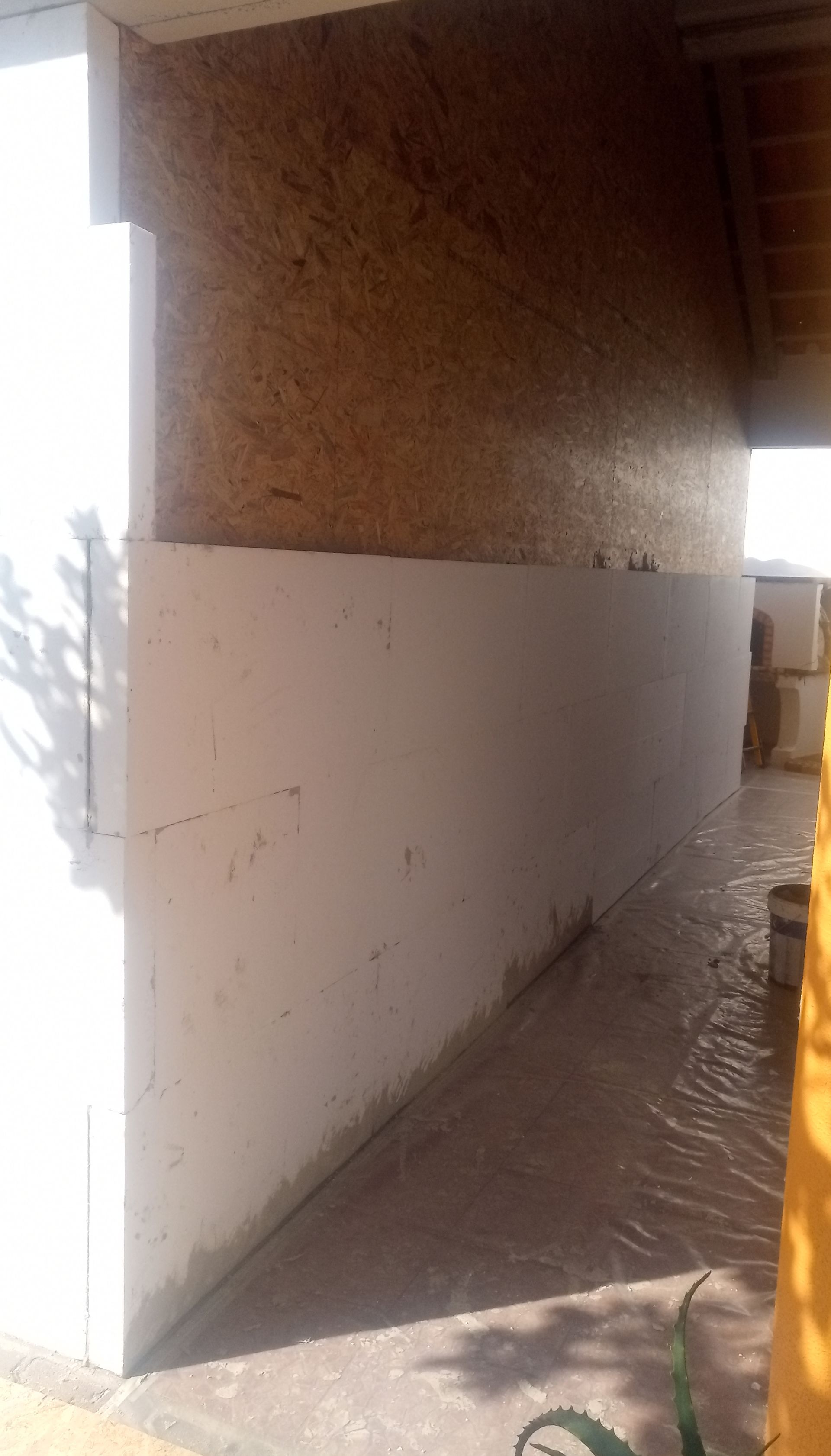 Parede branca com uma seção de placa OSB acima, ambiente externo.