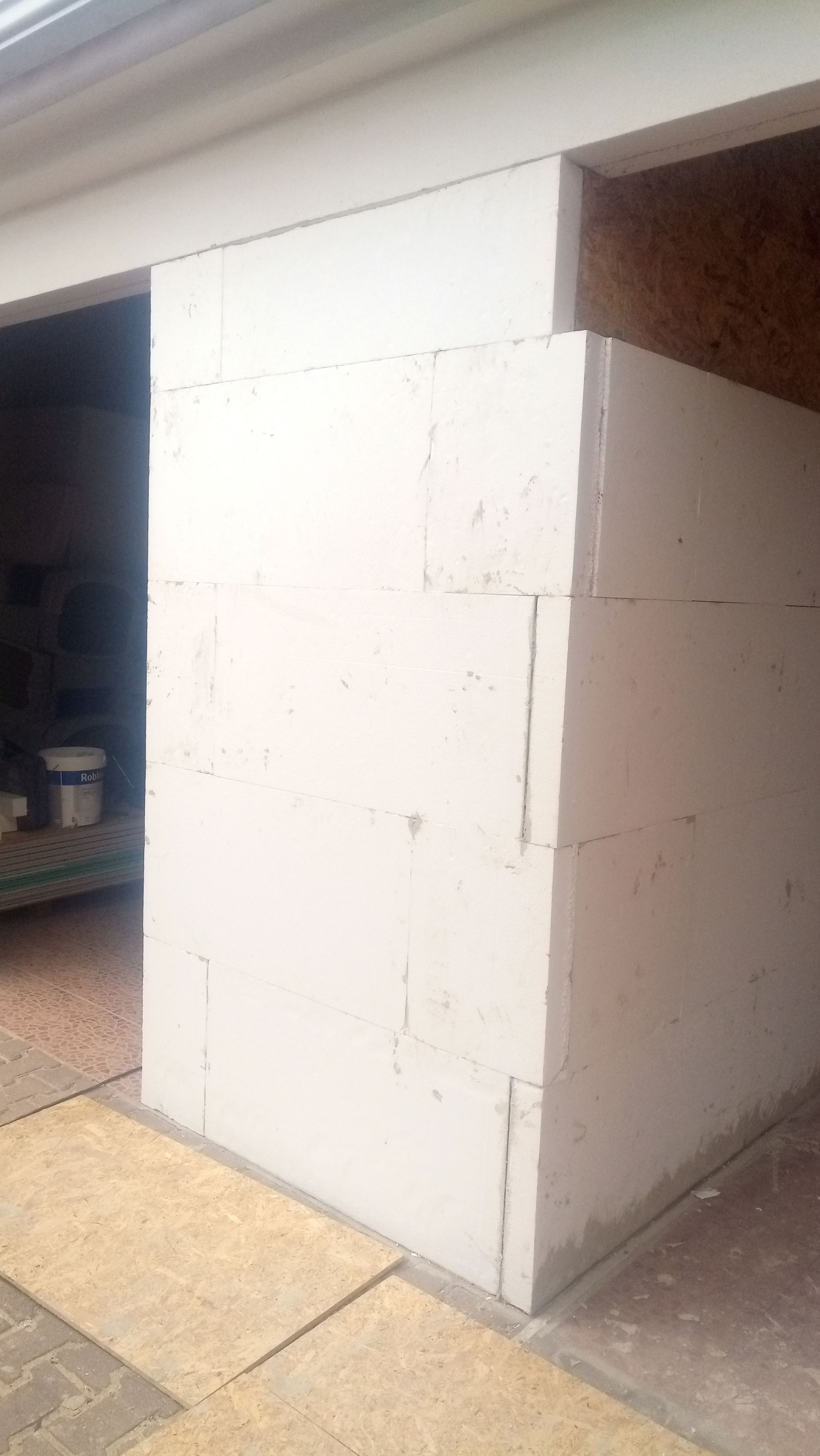 Construção de parede de blocos brancos, em ambiente interno. Piso de madeira clara, parcialmente acabado.