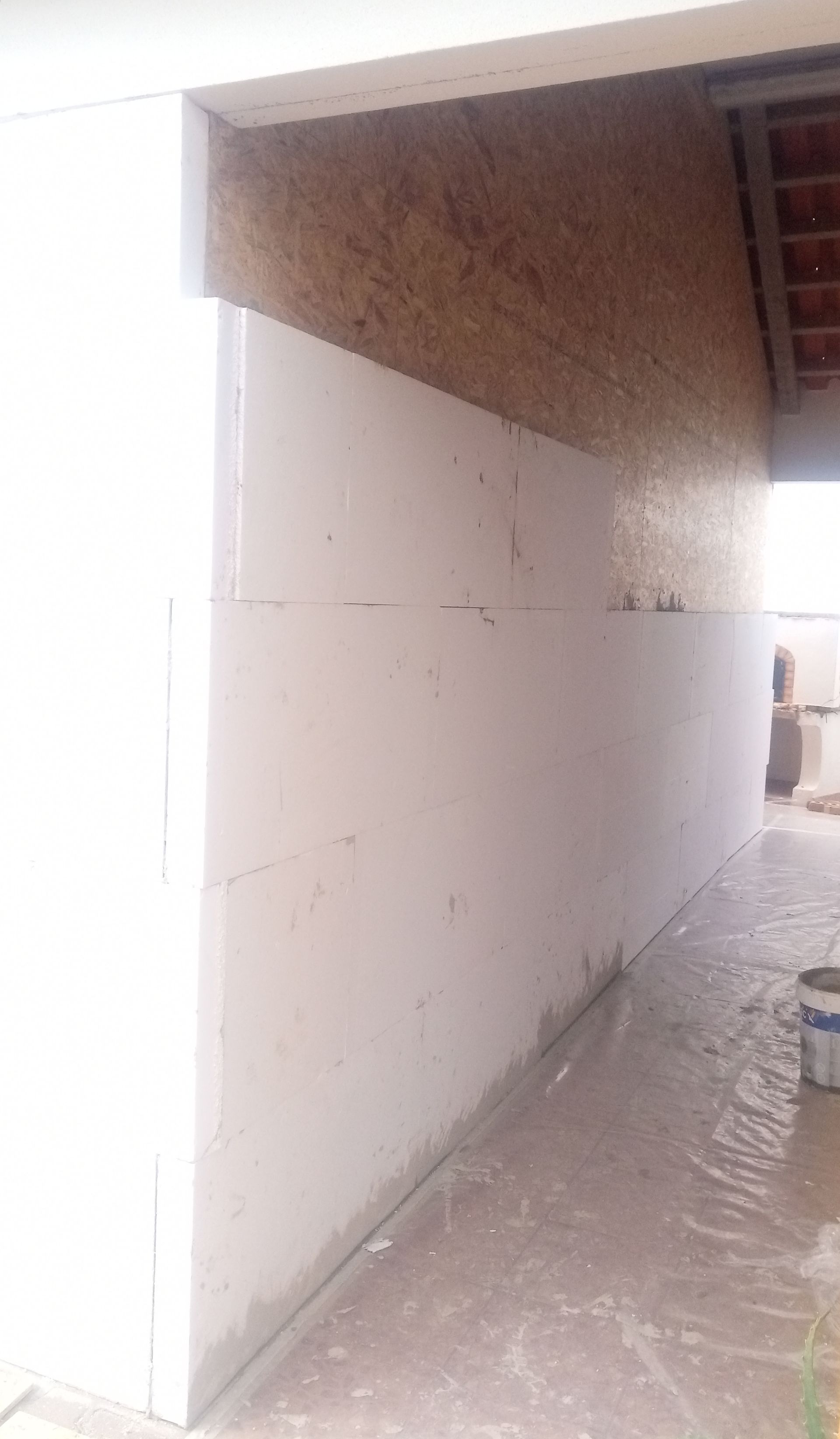 Parede branca sendo construída sob um teto de madeira marrom-claro. Concreto fresco na base.