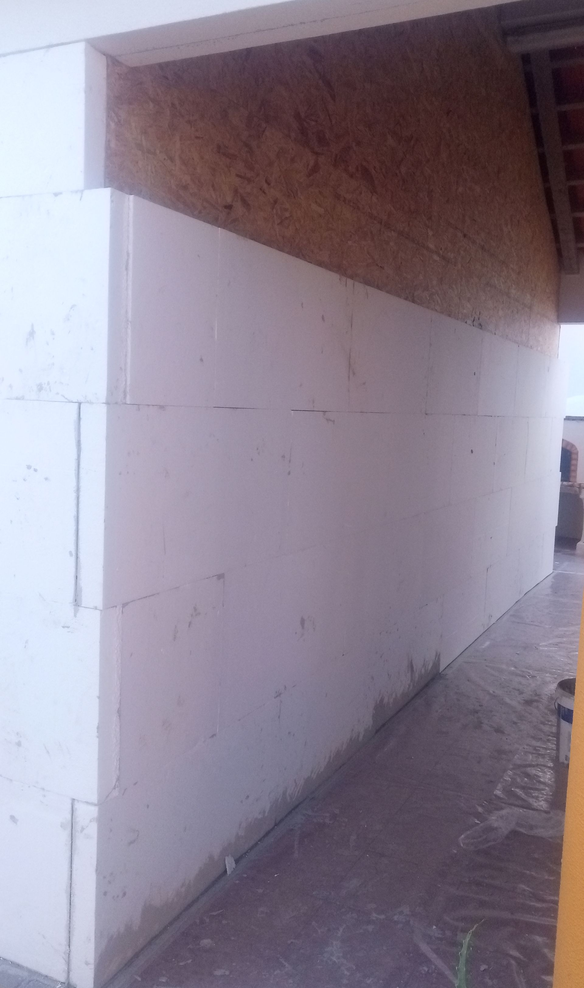 Blocos de isolamento de espuma branca formando uma parede, com painéis de madeira acima. Ambiente externo.