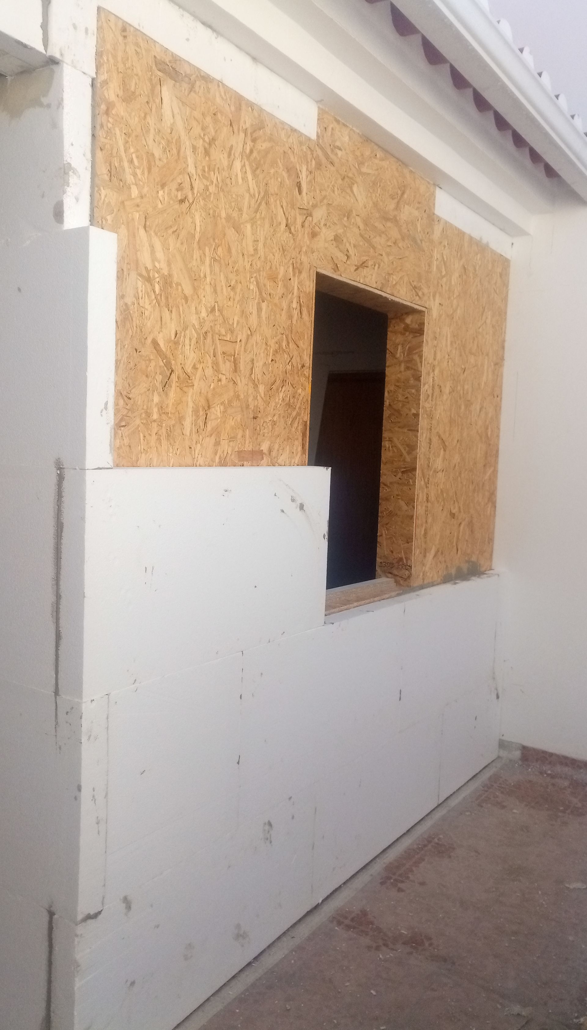 Parede externa com abertura para janela, revestida com painéis de partículas e isolamento branco.