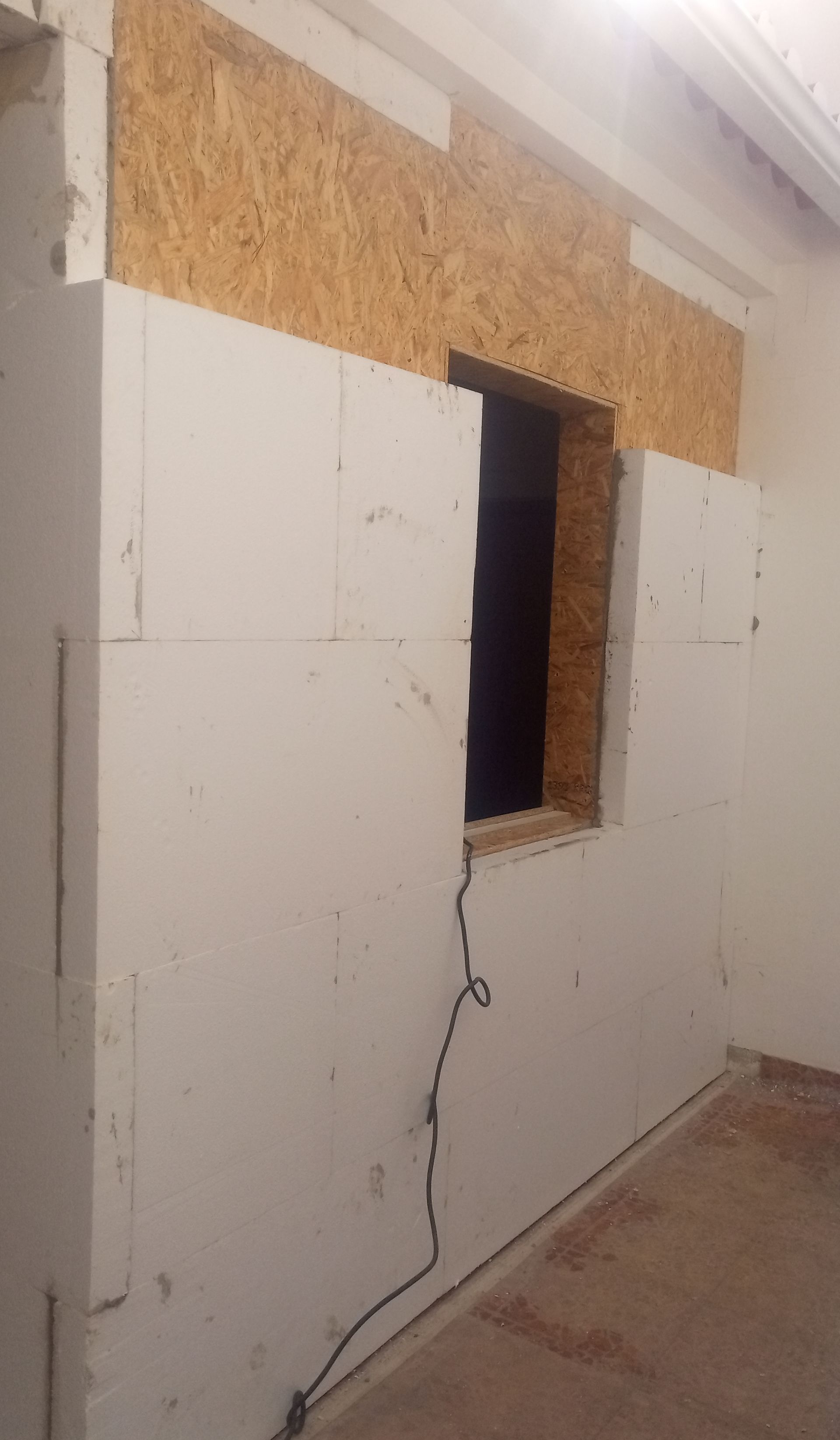 Construção da parede interna em andamento; painéis de isolamento branco instalados ao redor da abertura da janela, com revestimento de madeira acima.