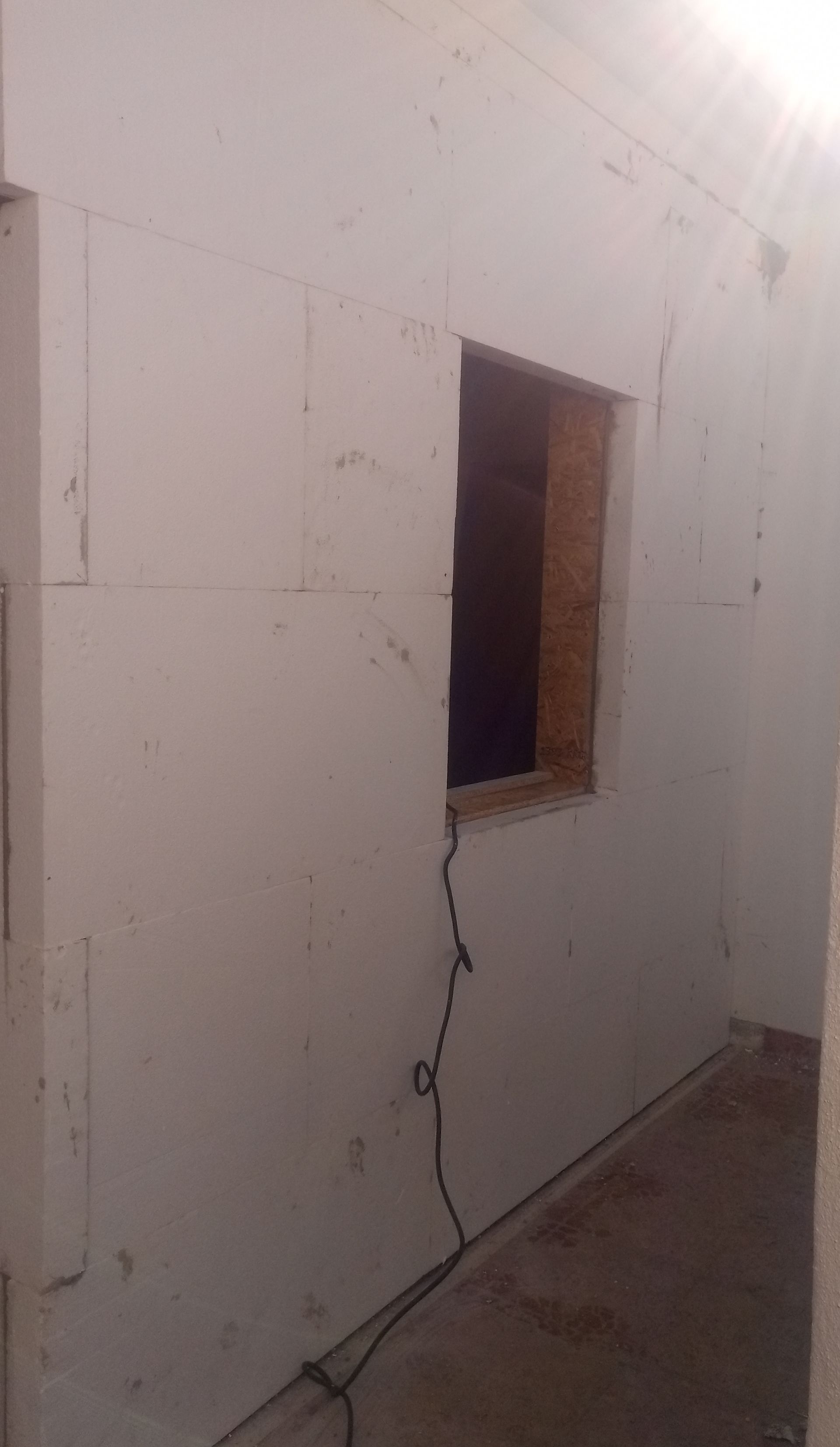 Interior de um quarto com paredes de blocos de espuma branca e uma janela.