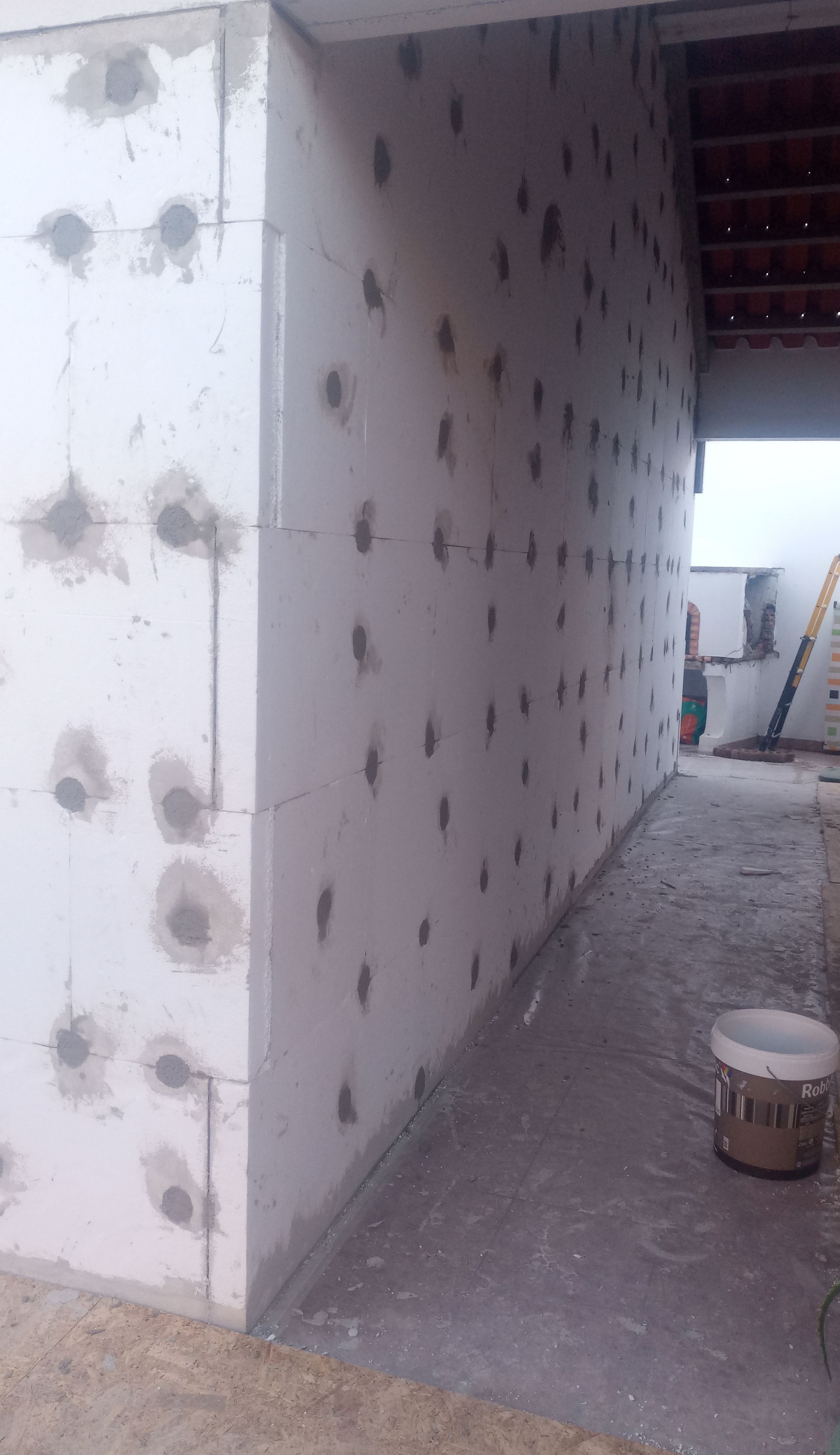 Construção de uma parede externa de edifício em blocos de isopor branco, com remendos de gesso cinza.