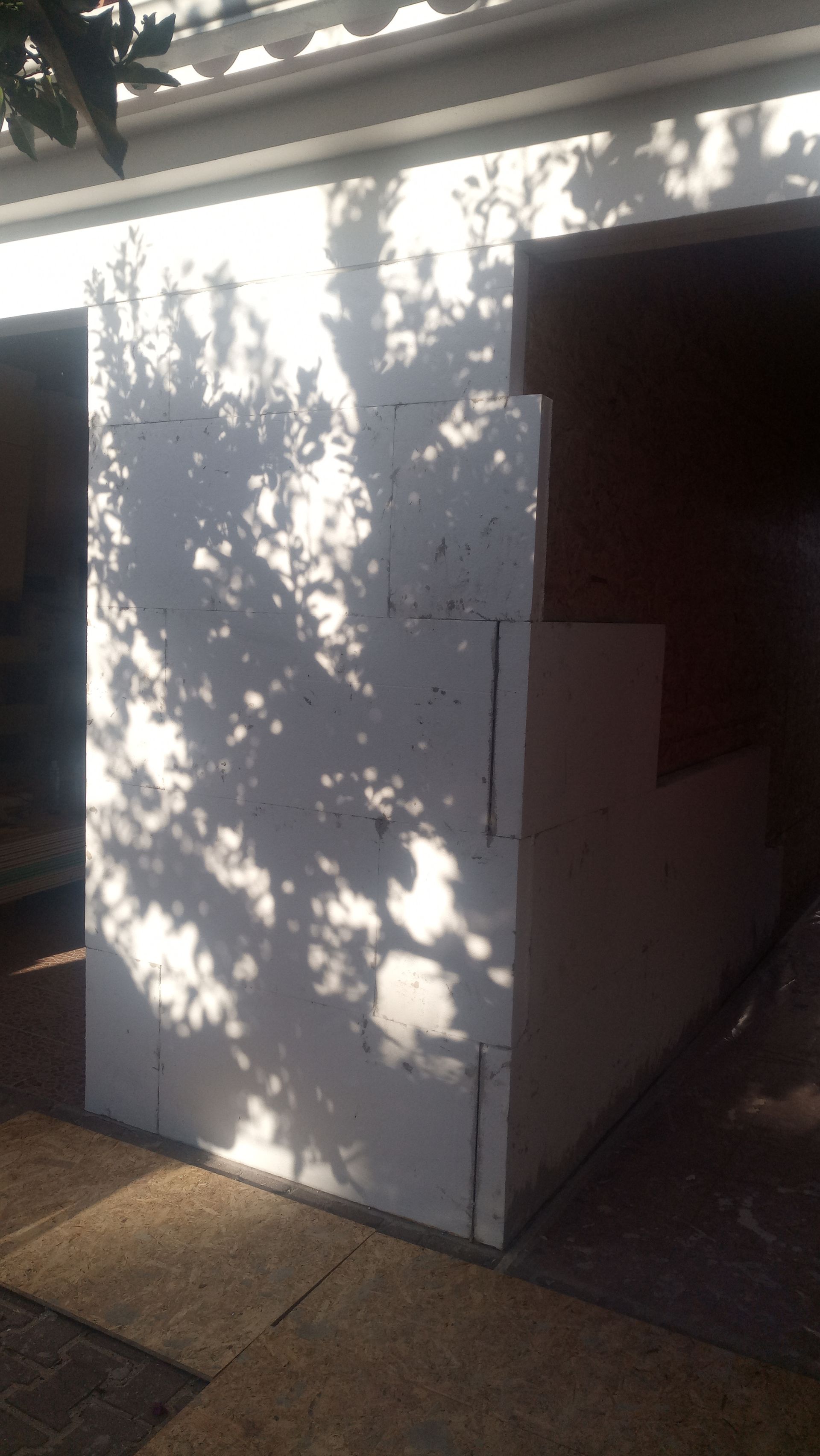 Parede de blocos de concreto branco em construção, com abertura para porta ou janela, na área externa.