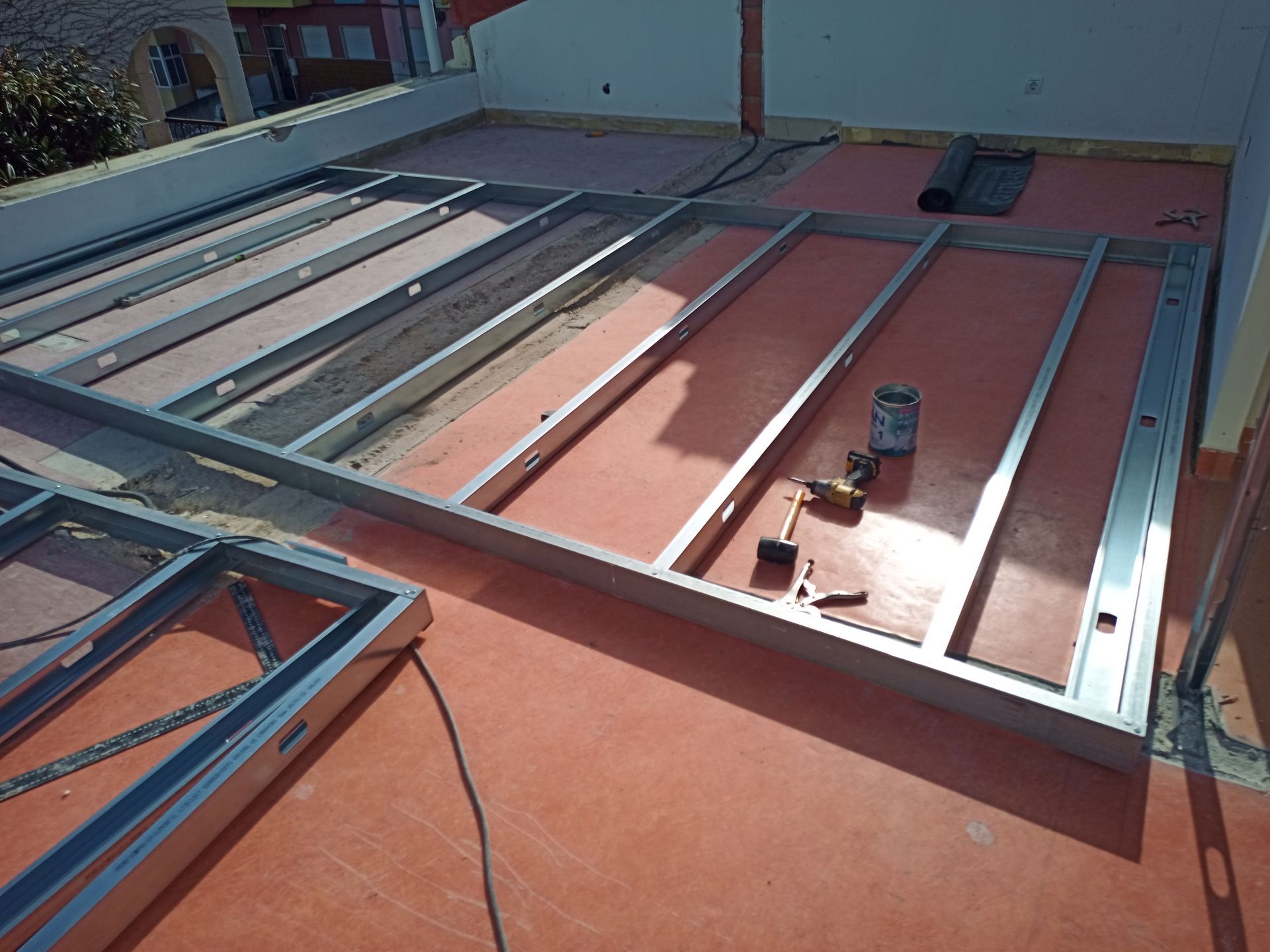 Estrutura metálica disposta sobre uma superfície vermelha, possivelmente para um projeto de construção em um telhado. Ferramentas estão presentes.