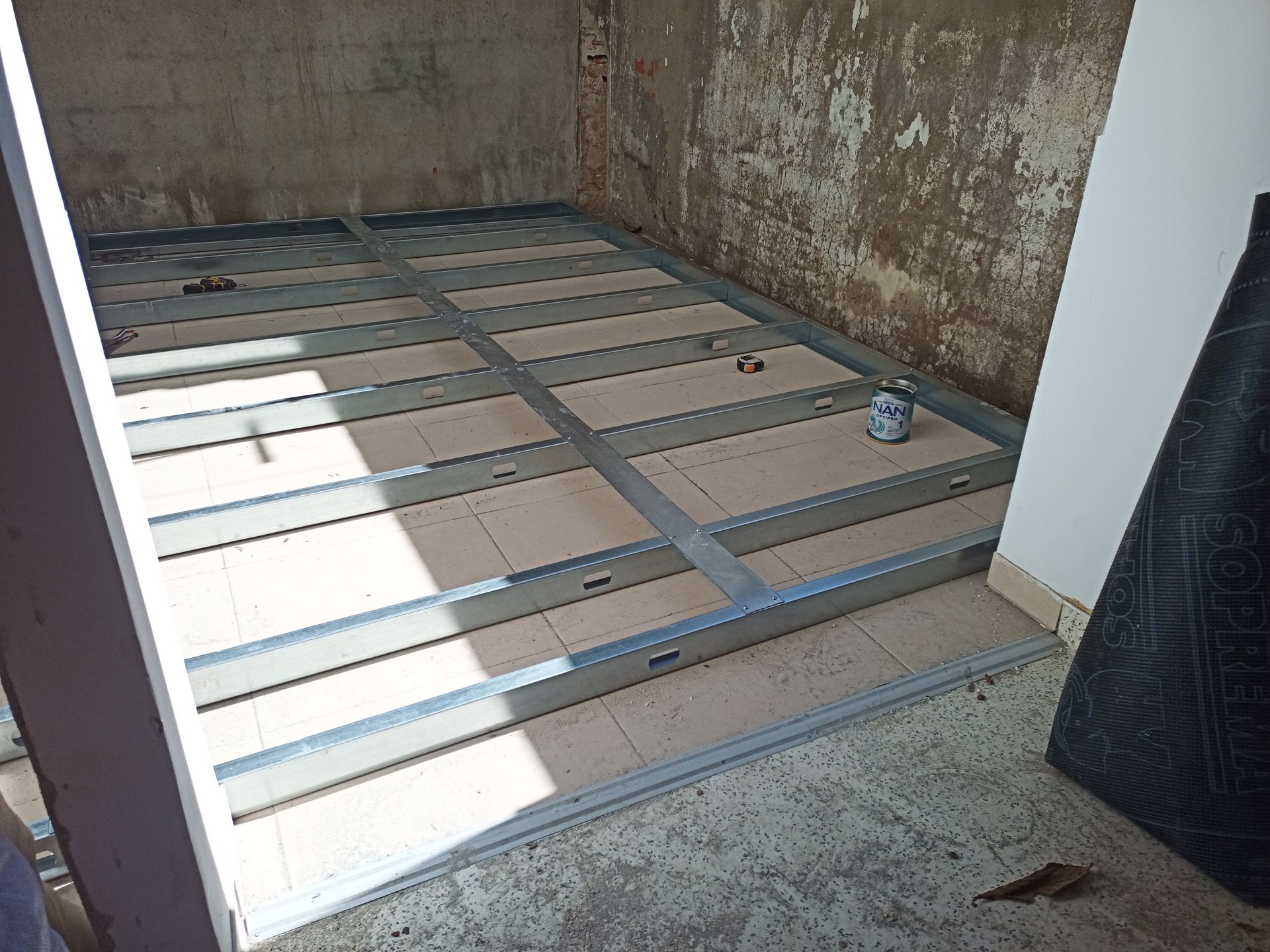 Construção com piso em estrutura metálica em um cômodo, com isolamento marrom e paredes de concreto claro.