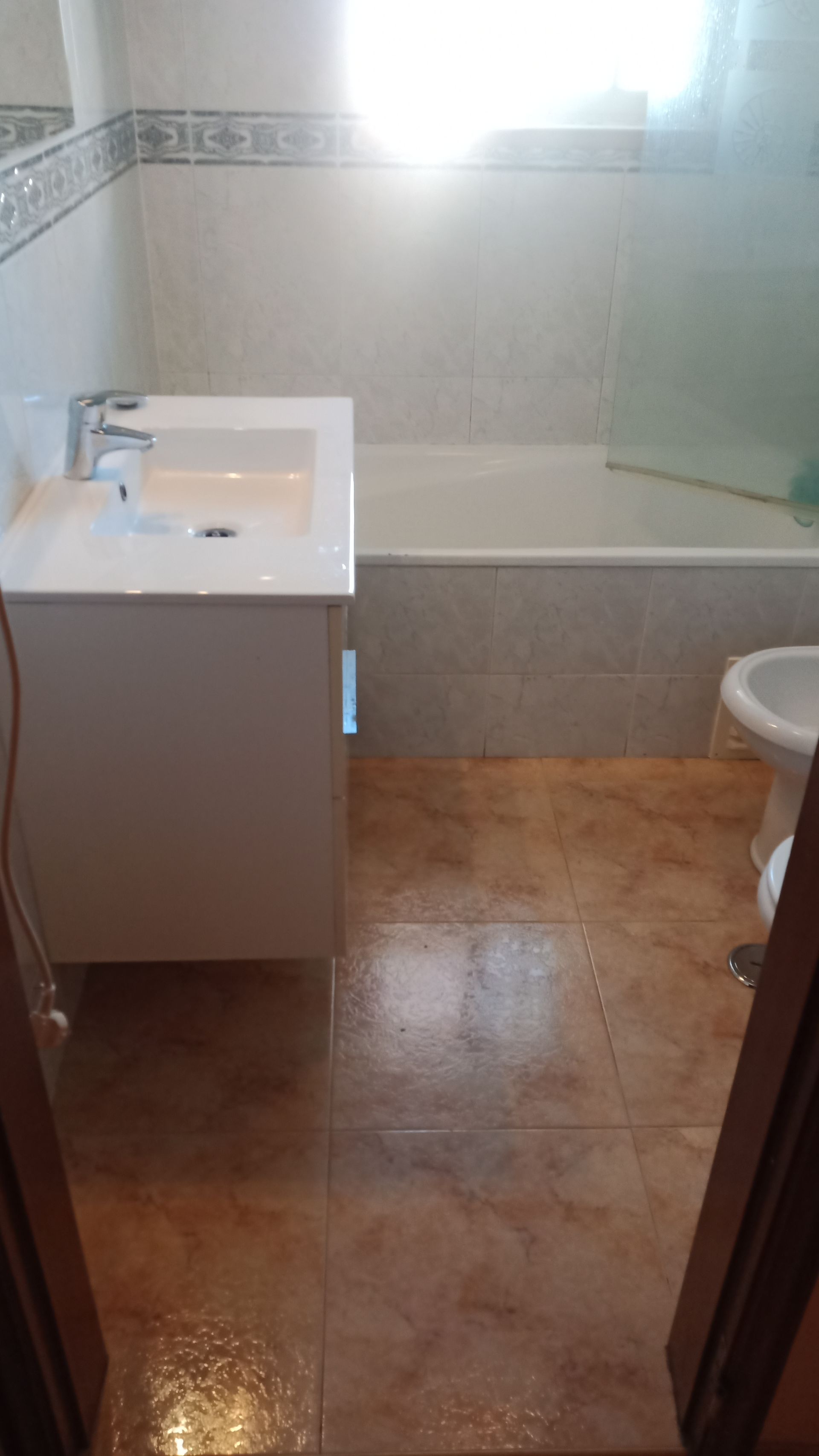 Banheiro com pia e armário brancos, banheira, vaso sanitário e piso de azulejo marrom.