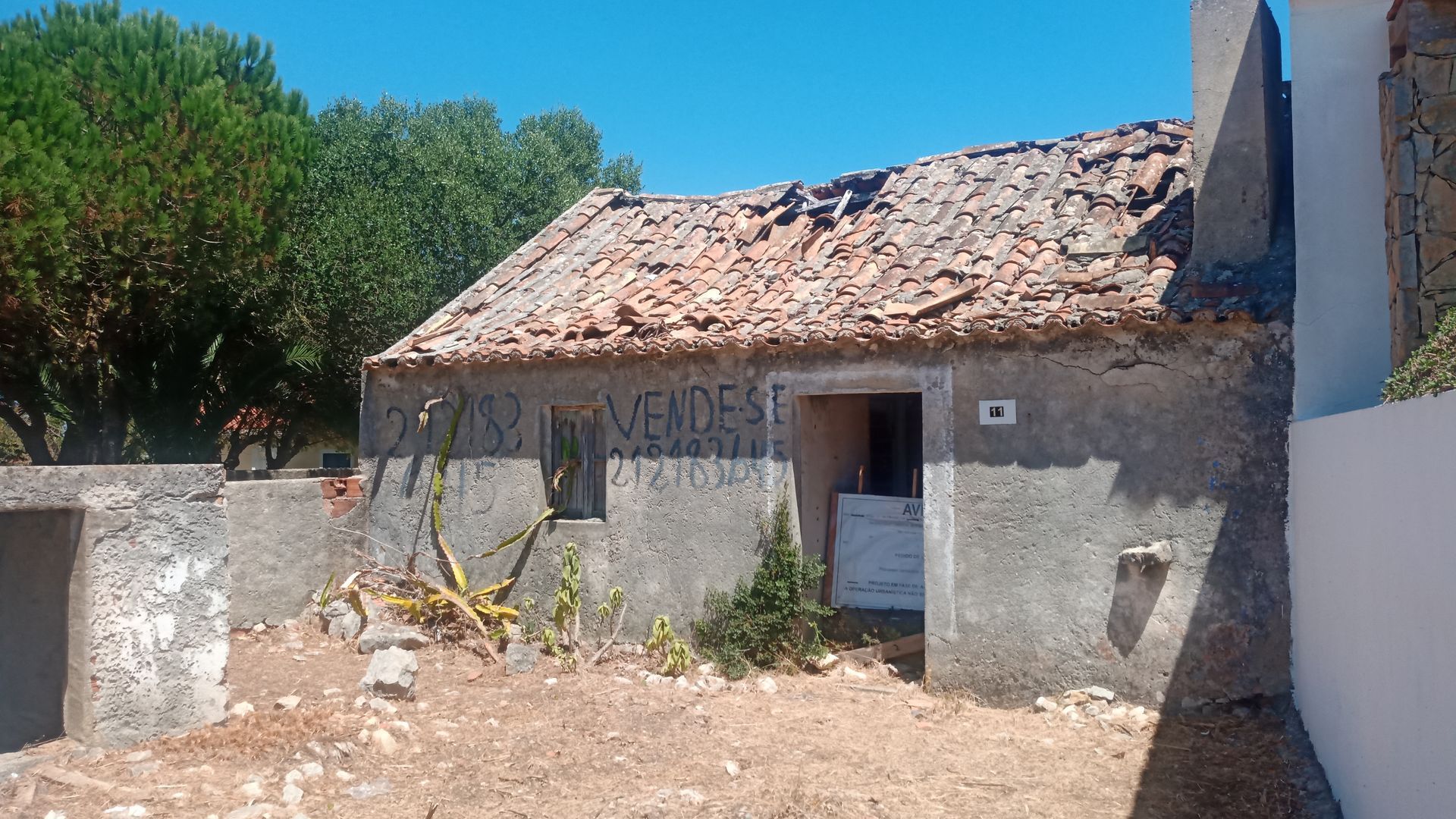 Prédio de concreto dilapidado com telhado de telhas vermelhas e a inscrição 