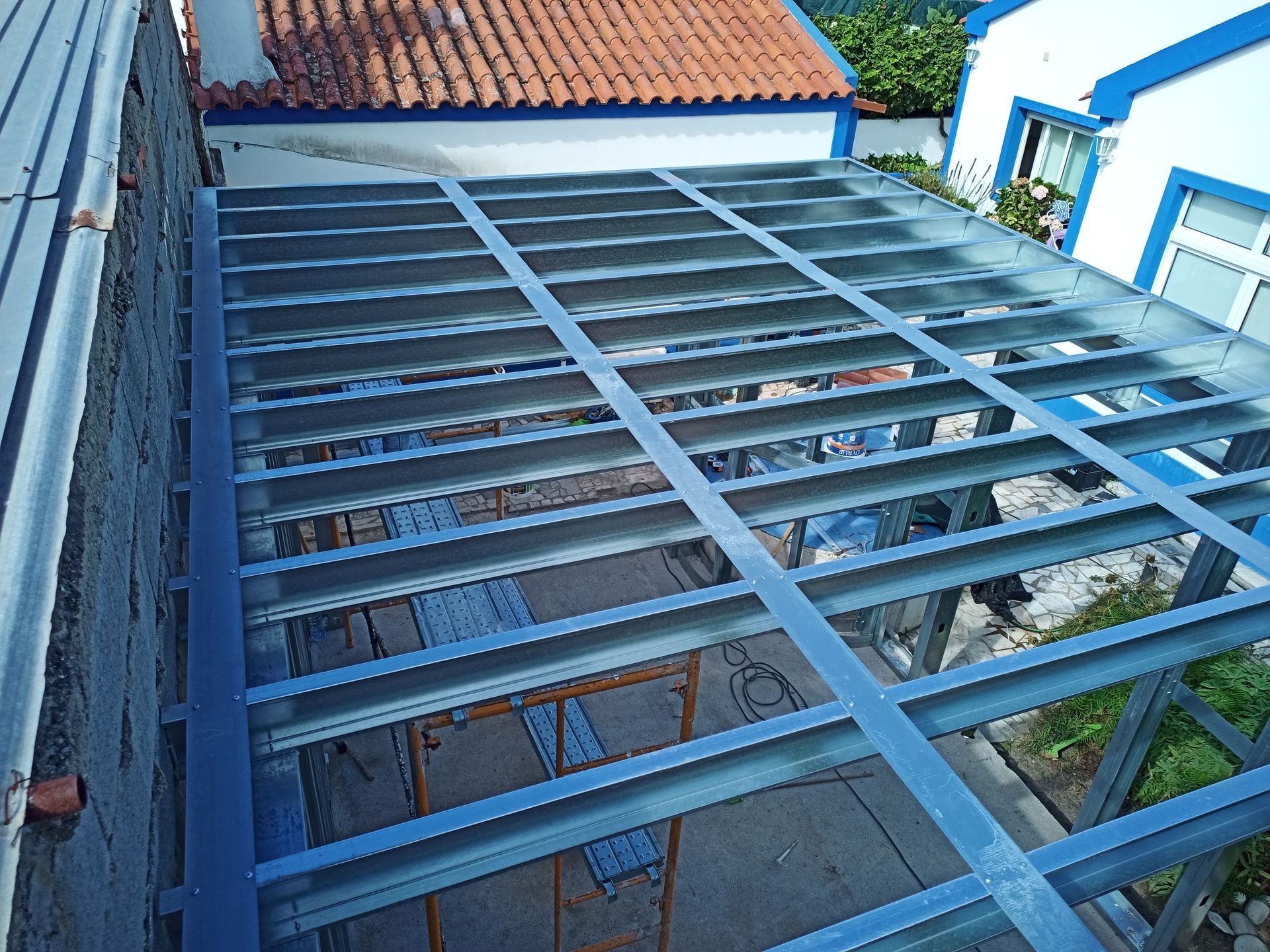 Estrutura metálica com cobertura transparente, anexada a um edifício, vista de cima.