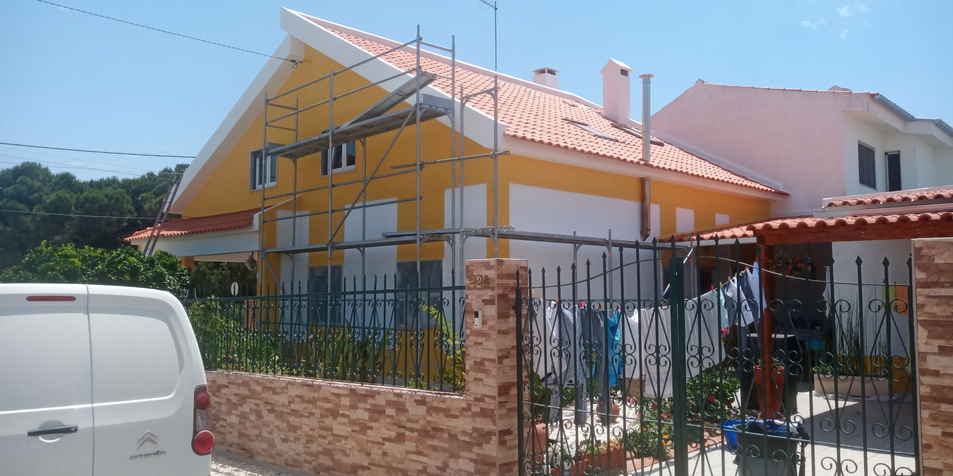 Casa amarela com telhado de telha vermelha, andaimes e uma van branca na frente.