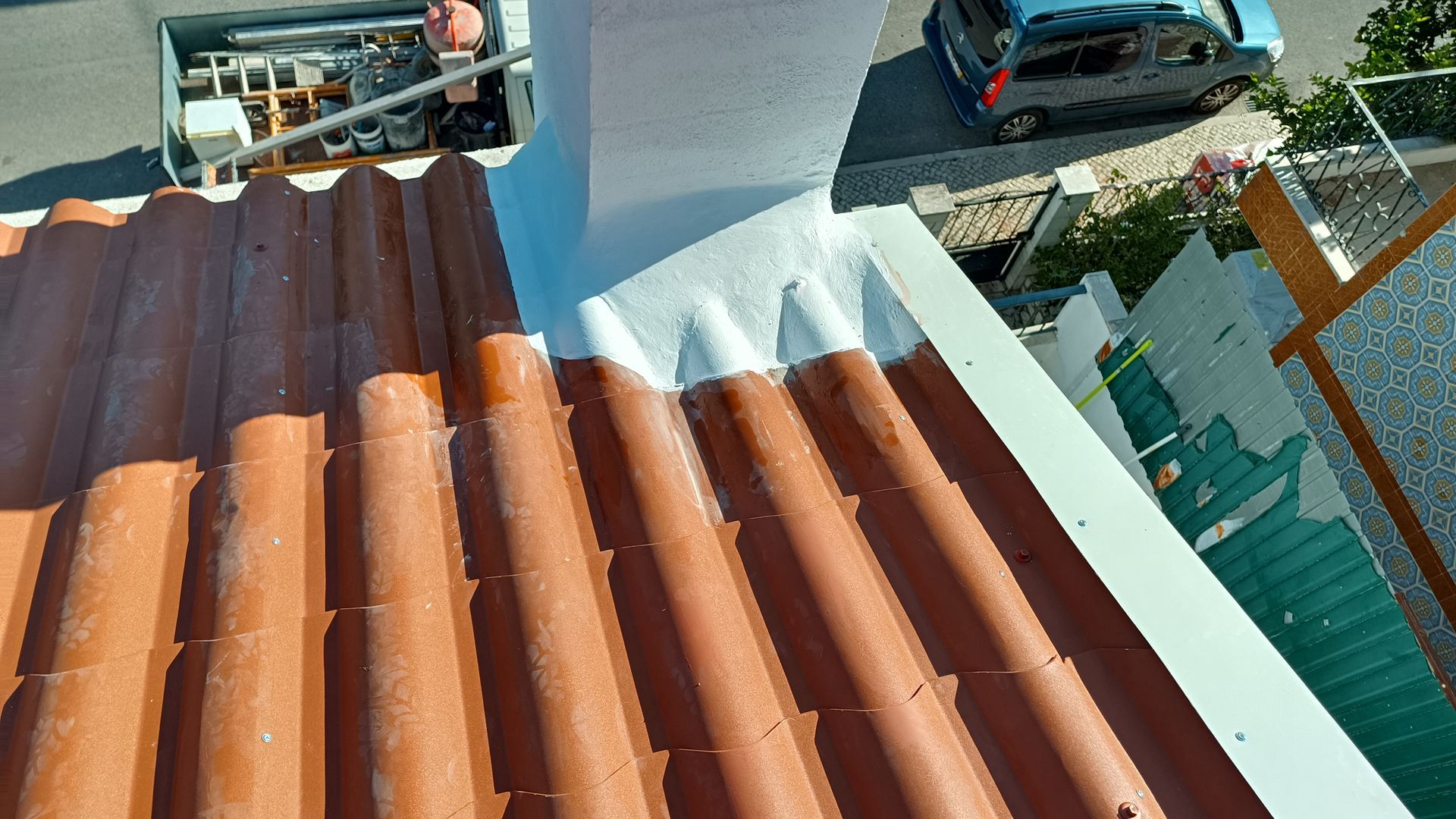 Telhado com telhas laranja ao lado de uma estrutura branca; um carro é visível ao fundo.