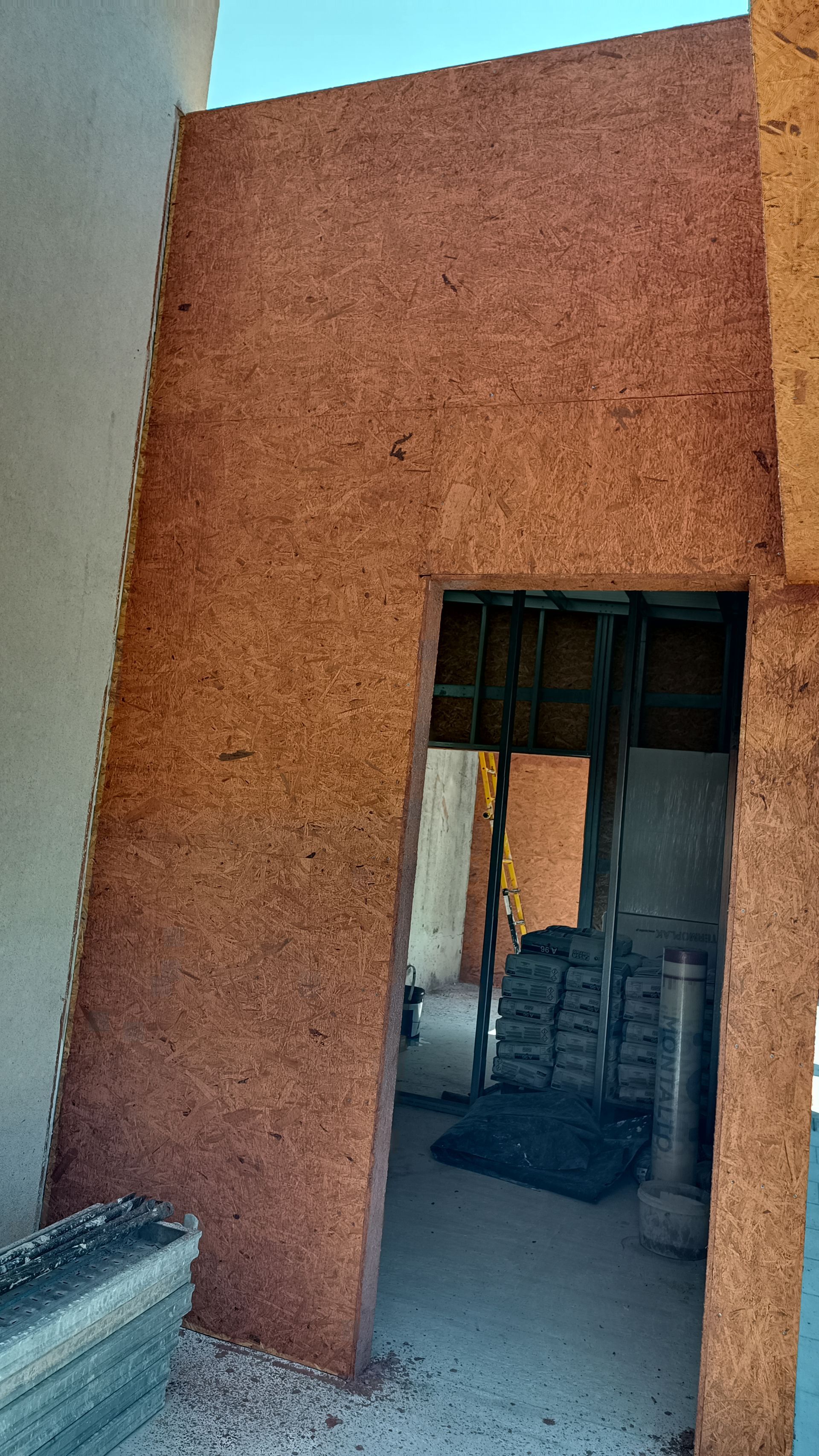 Parede de aglomerado marrom com porta, em um canteiro de obras.