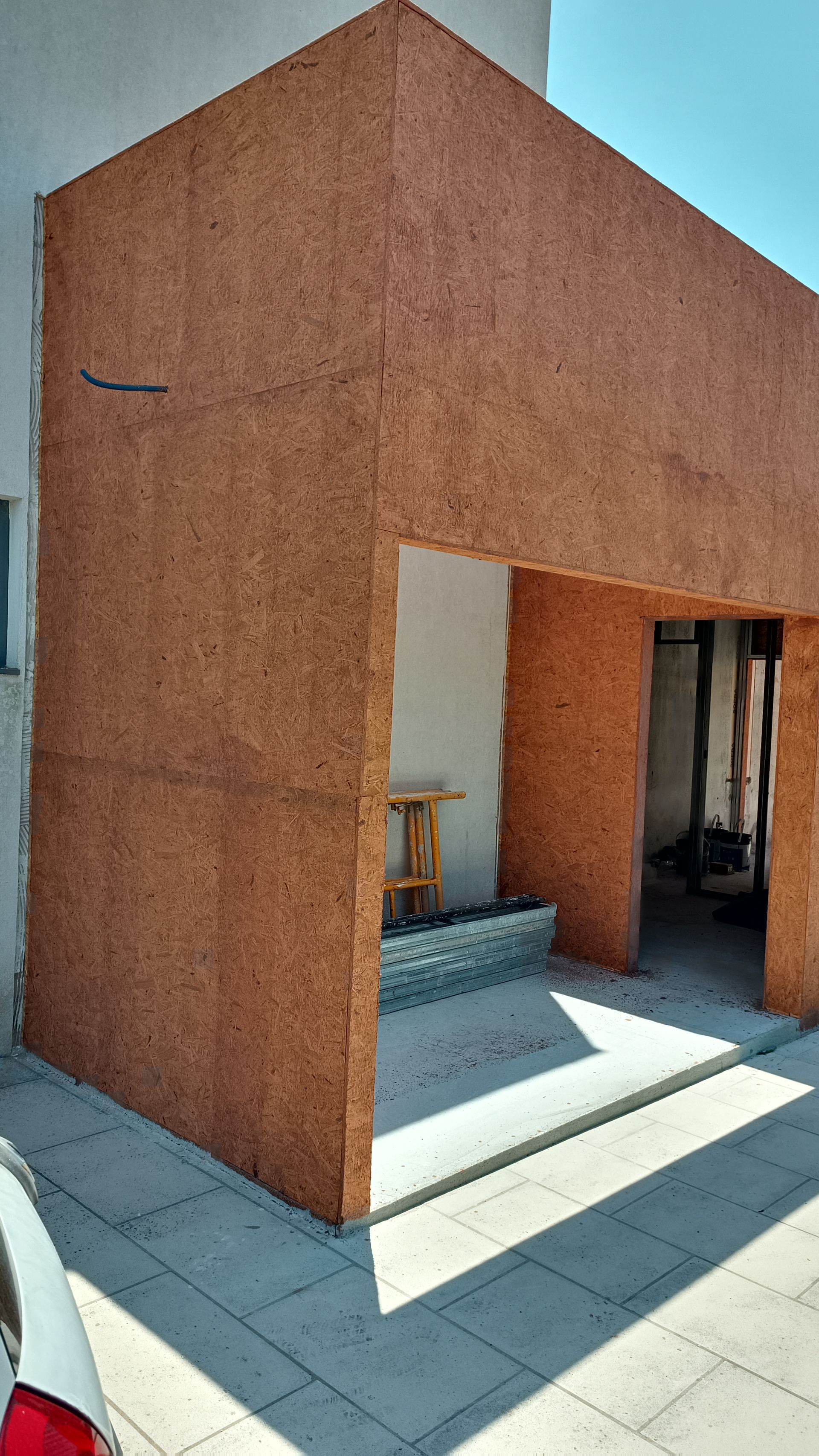 Exterior do edifício com fachada de madeira marrom, porta aberta e base parcial de pedra.