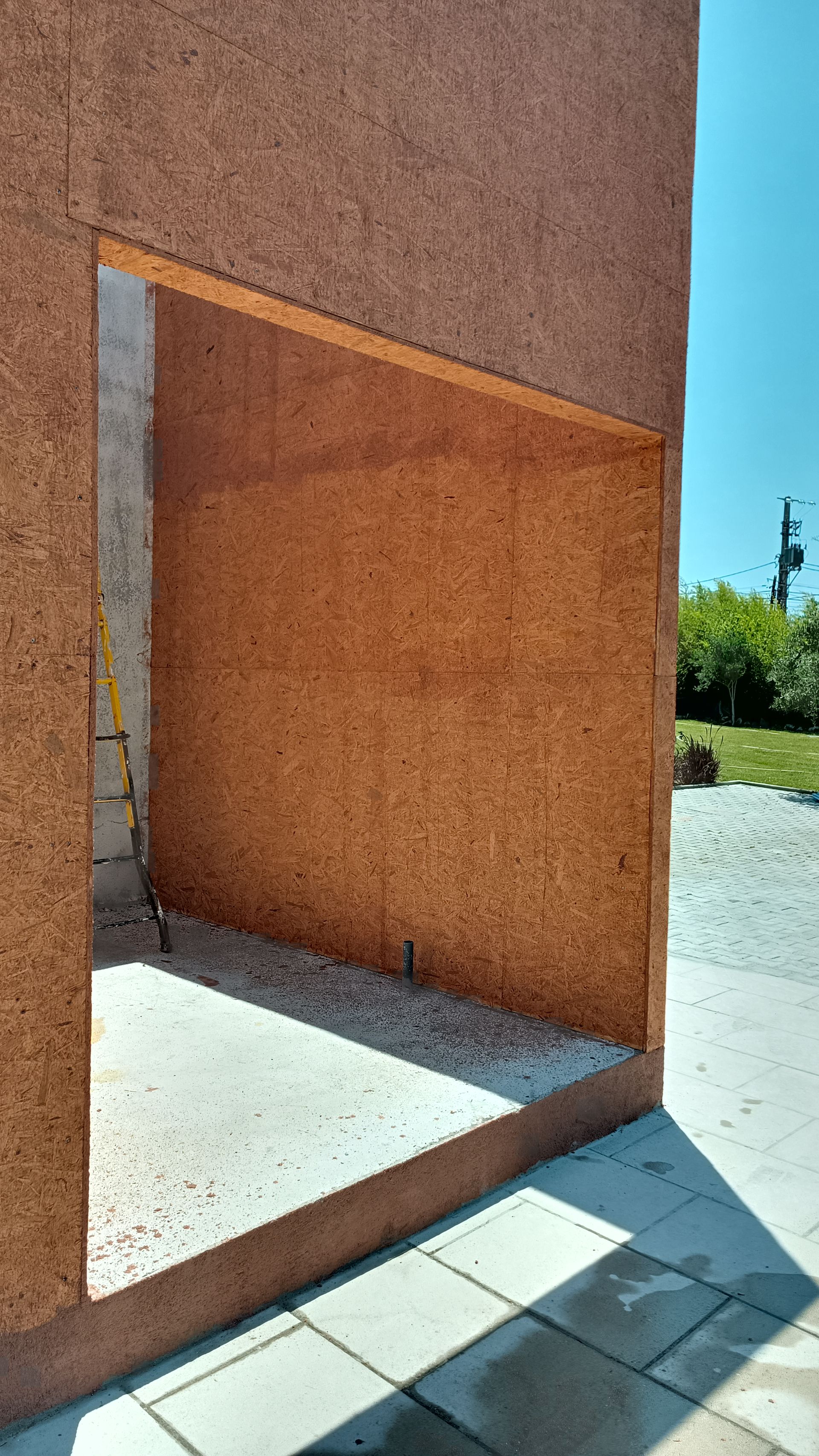 Parede externa com uma abertura que revela um interior de concreto; a parede é de um tom marrom quente.