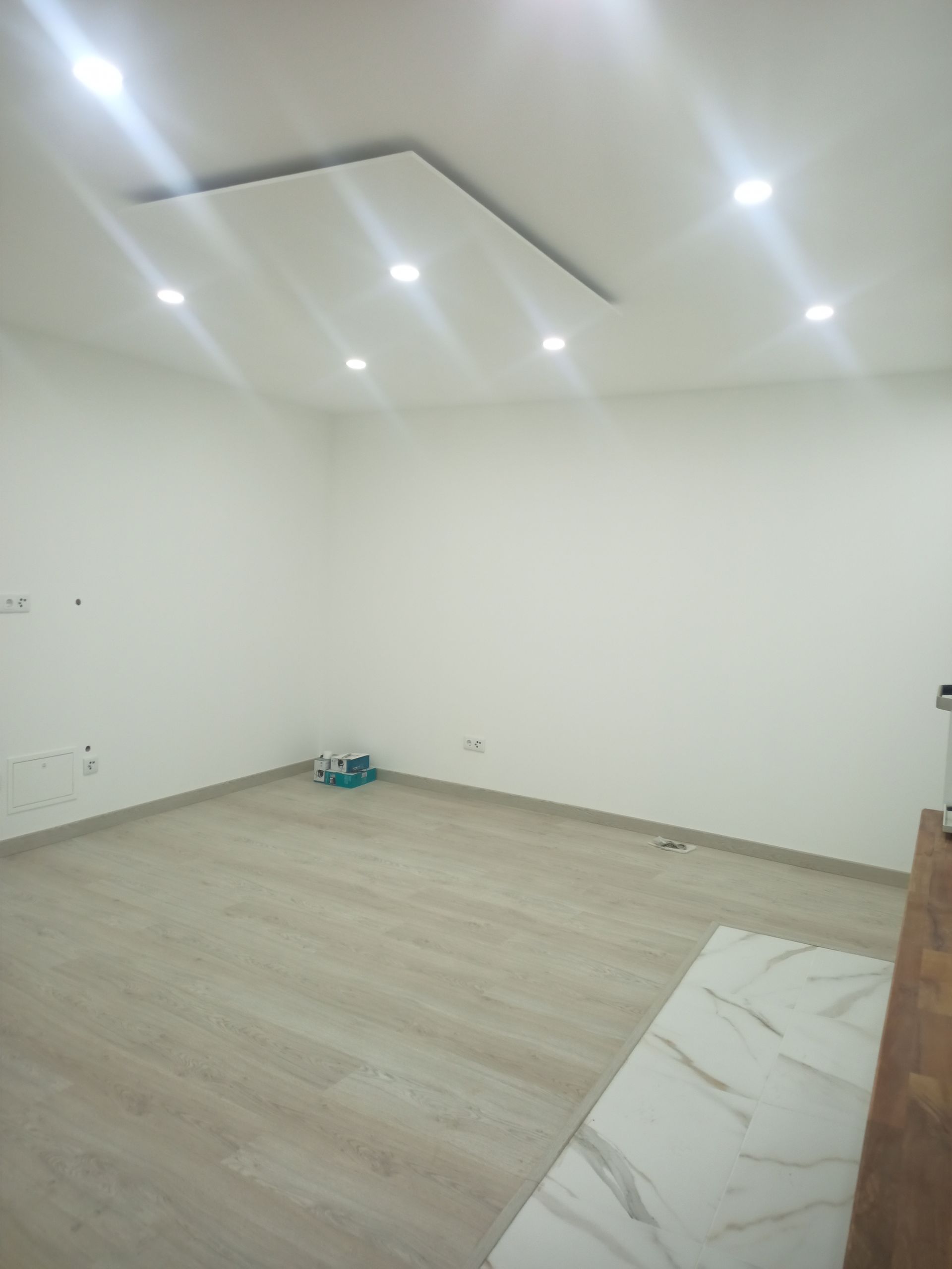 Quarto vazio com paredes brancas, iluminação embutida e piso que imita madeira clara.