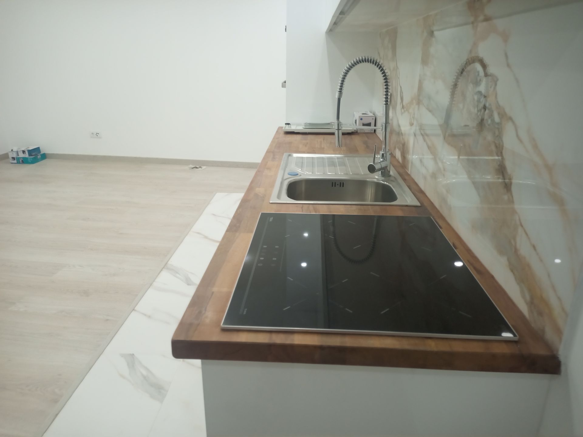 Bancada de cozinha com pia, fogão e torneira, com backsplash em padrão de mármore, armários brancos e bancada de madeira.