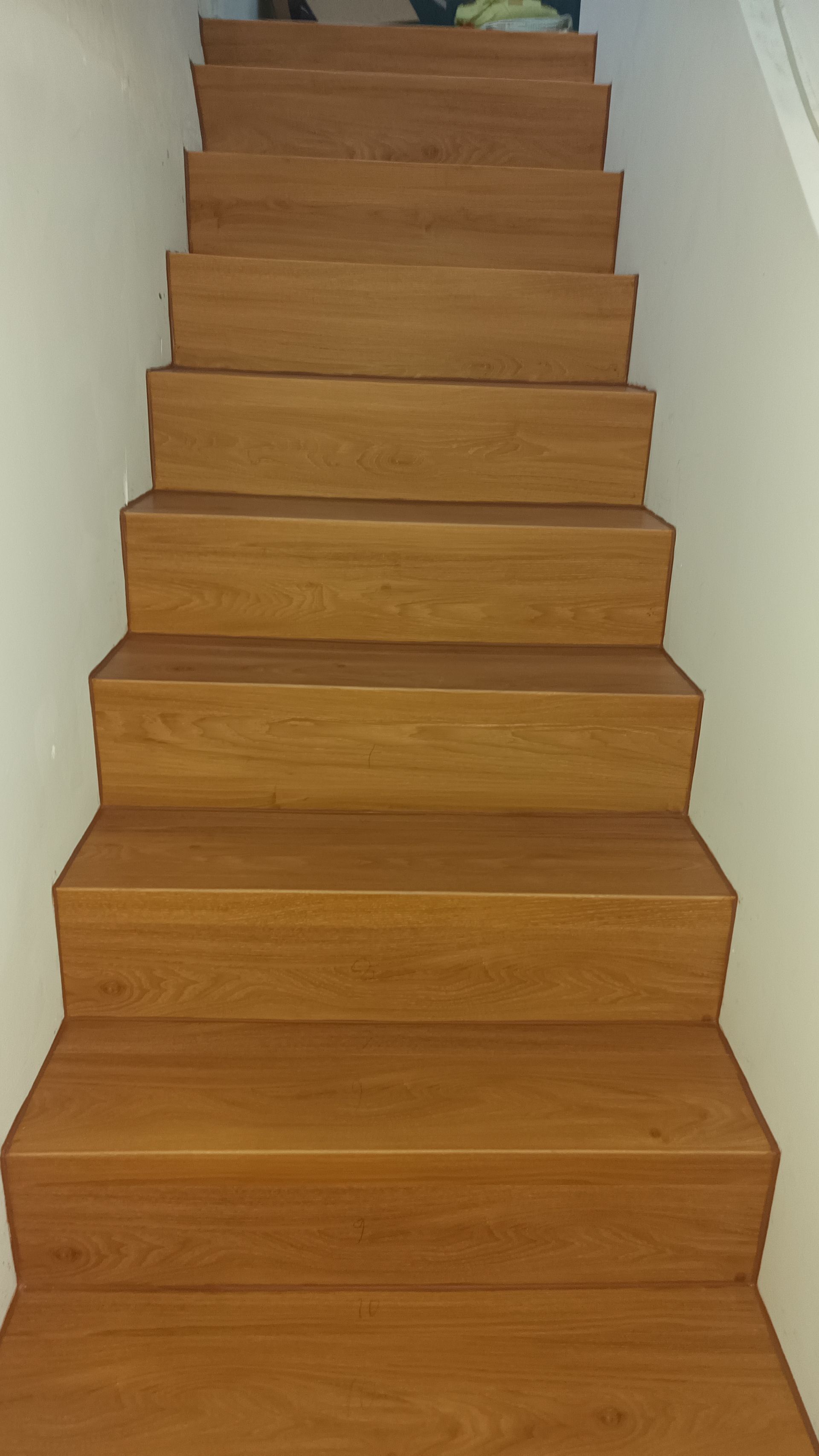 Escada de madeira com degraus castanho-claros e paredes brancas.