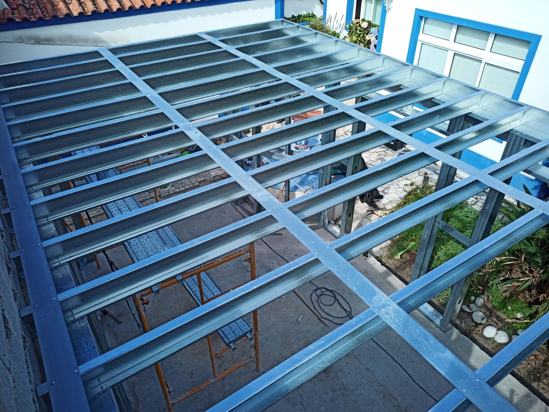 Estrutura metálica de um telhado parcialmente construído sobre uma área de pátio.