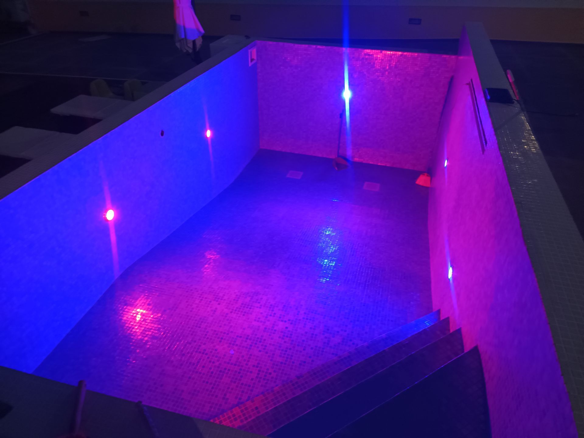 Piscina vazia com luzes azuis e rosas iluminando o interior e os degraus.