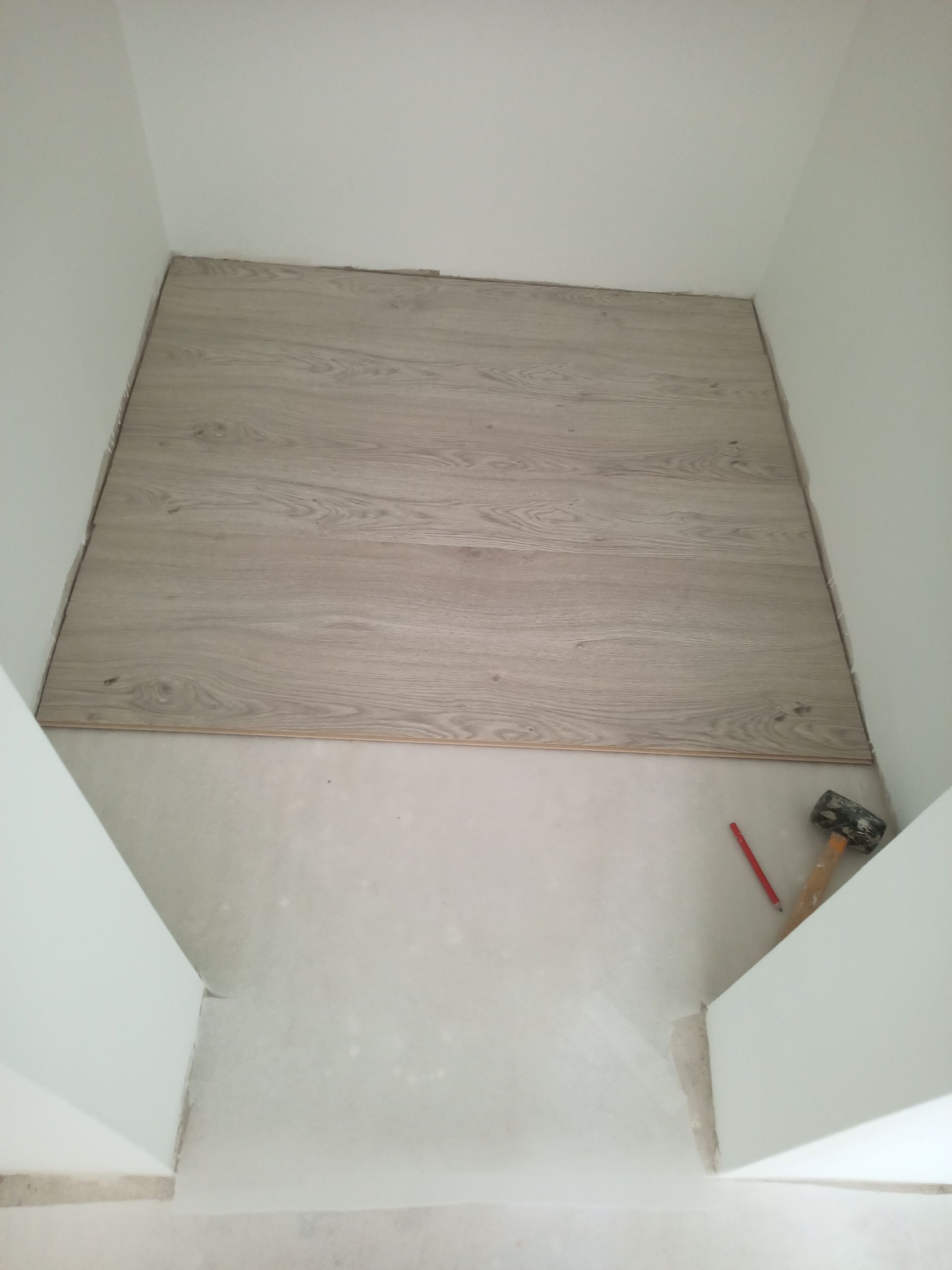 Obra de piso em andamento. Azulejos imitando madeira bege assentados na entrada; paredes brancas ao redor.