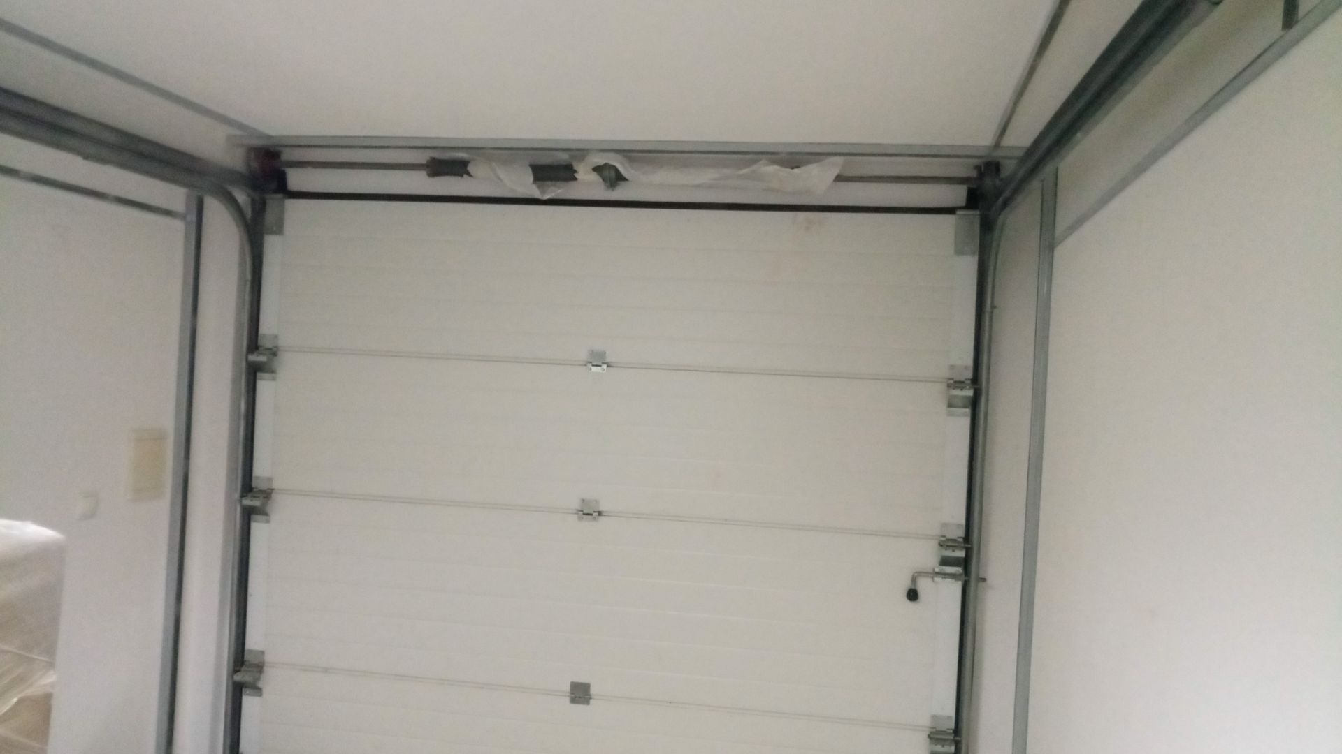 Vista interna de uma porta de carga branca, com dobradiças e estrutura metálica. A porta está fechada.