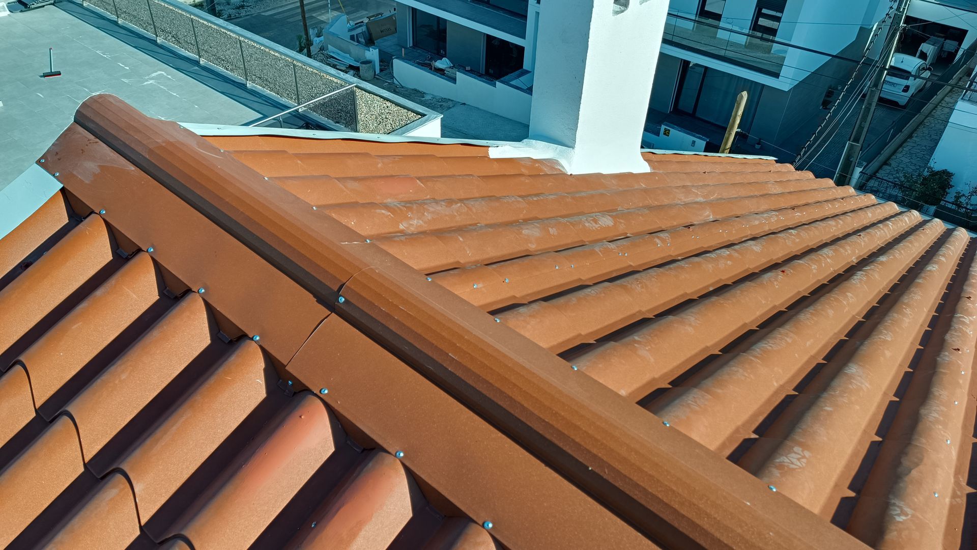 Telhado de telhas de terracota com uma chaminé branca e edifícios ao fundo.