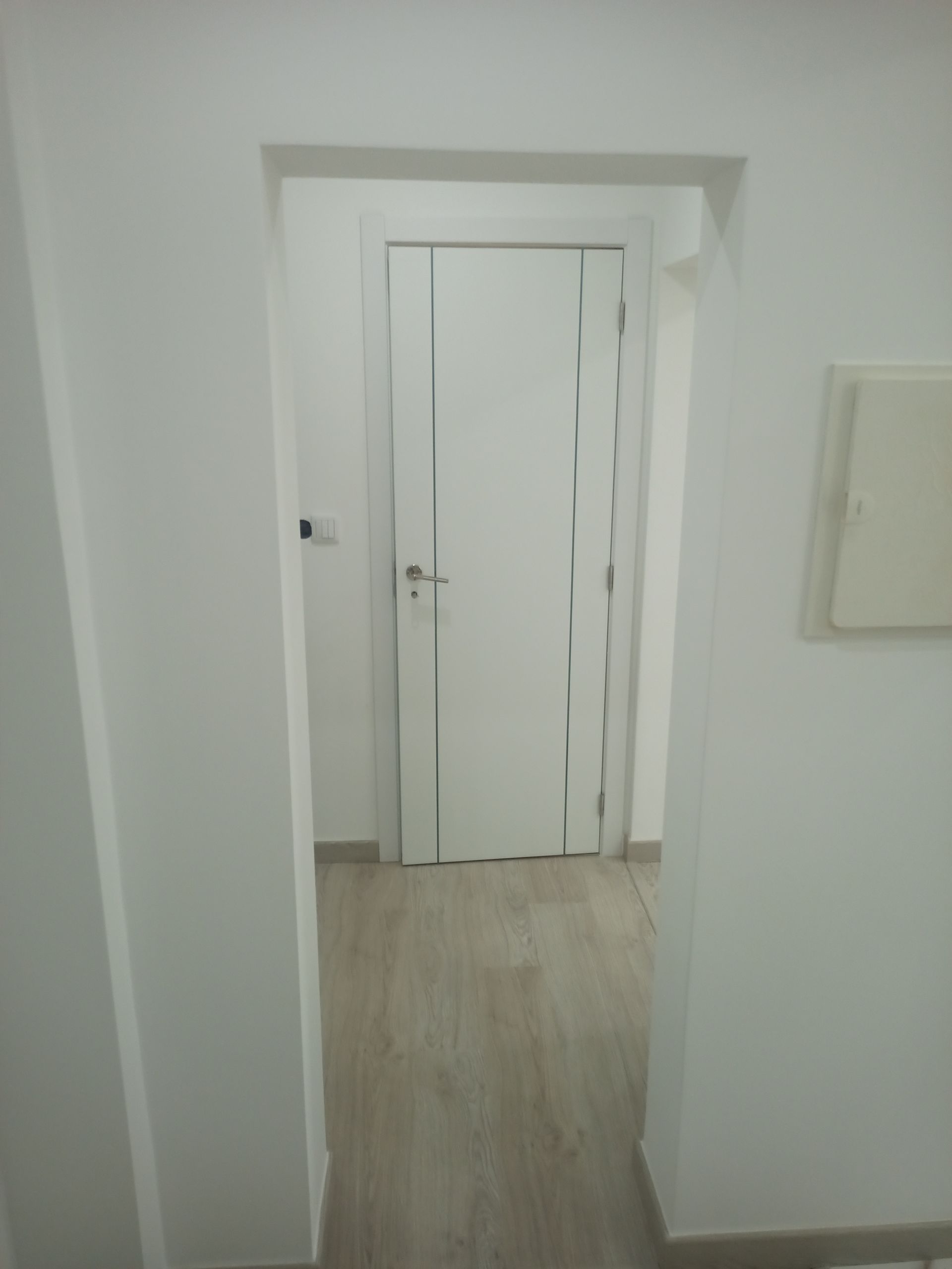 Porta interna branca em um vão de entrada branco, com paredes brancas e piso de madeira clara.