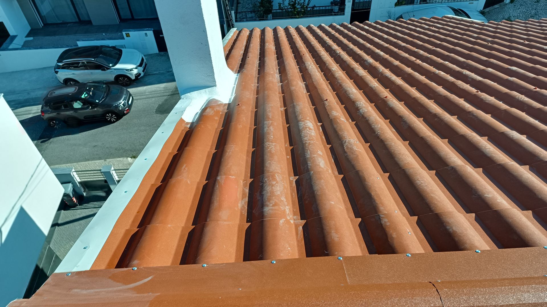 Telhado de zinco marrom com detalhes em branco. Carros estacionados na rua.