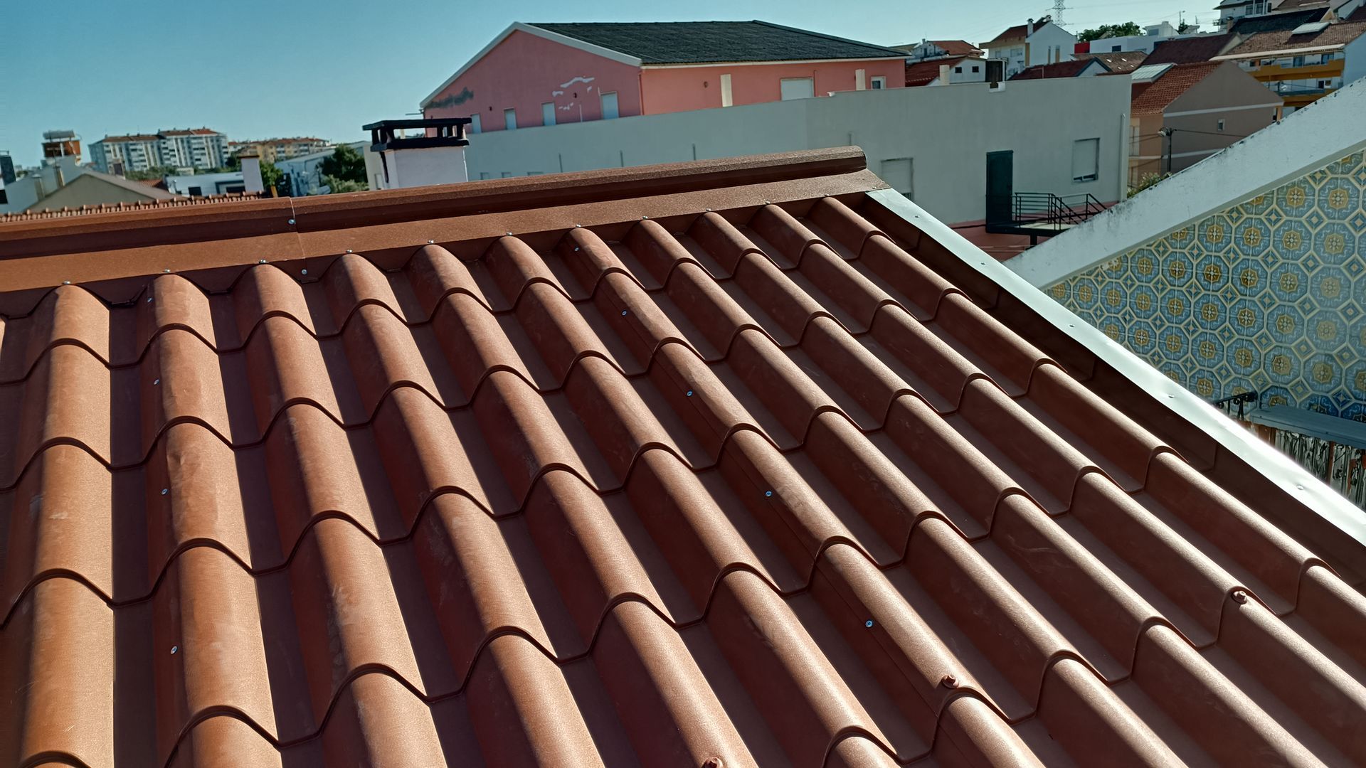 Telhado de telha de barro com edifícios ao fundo em um dia ensolarado.