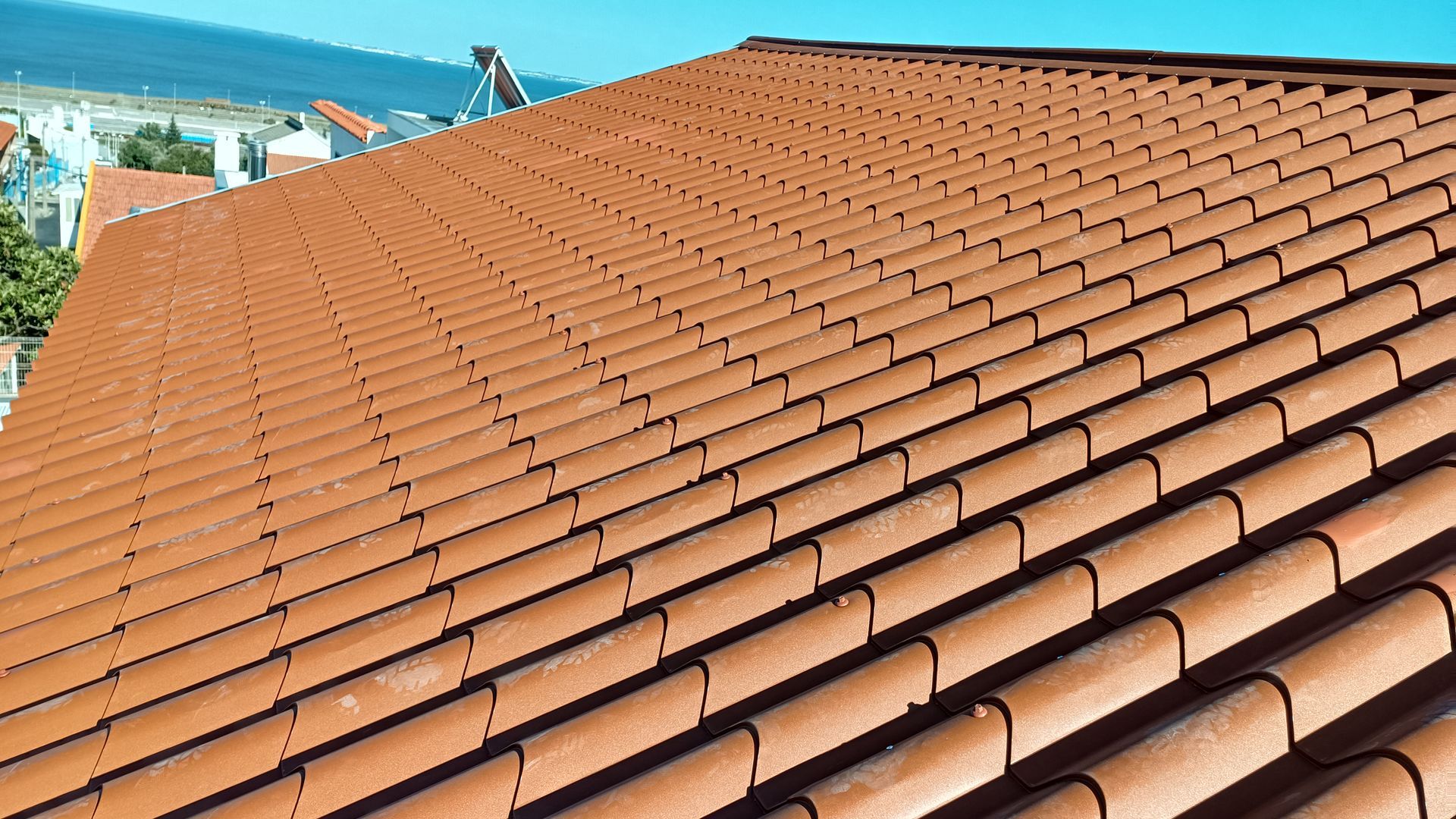 Telhado de telha de barro vermelha com uma ligeira curvatura, em ambiente urbano.