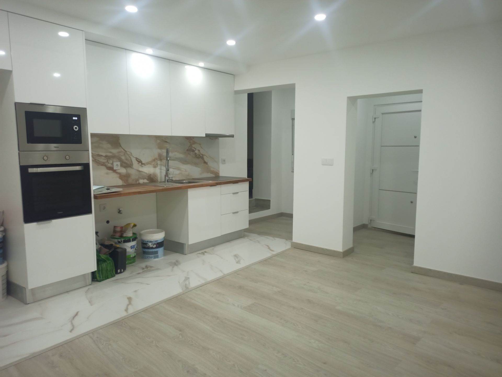 Cozinha moderna branca com eletrodomésticos embutidos, backsplash de mármore e piso de madeira clara.