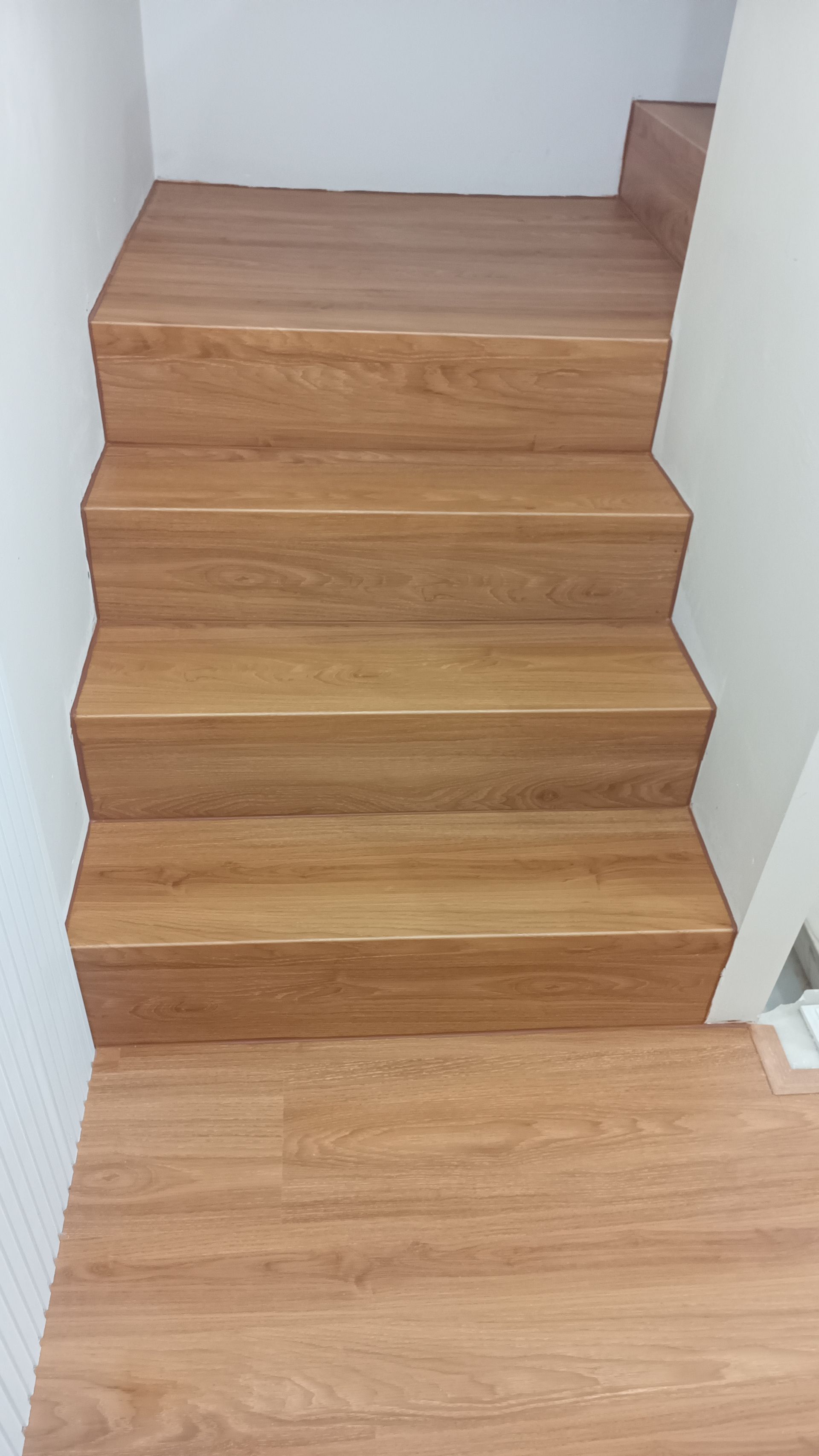 Escada de madeira que leva ao andar superior, com quatro degraus visíveis. As paredes são brancas.