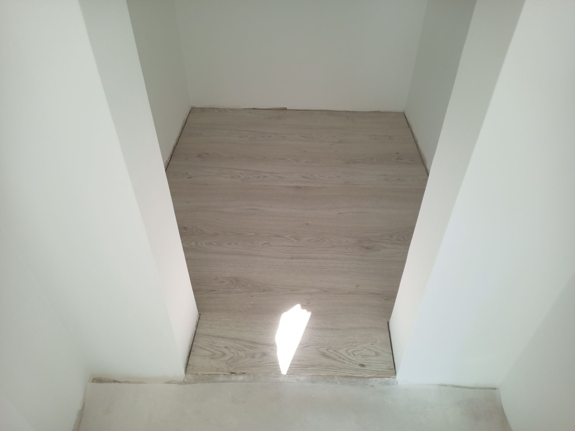 Piso com aparência de madeira clara instalado em um nicho entre paredes brancas.