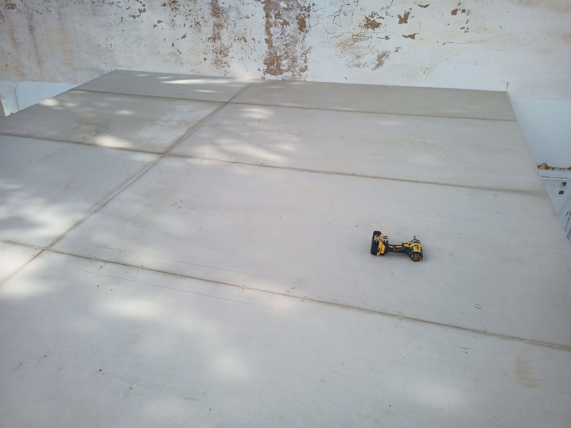 Um pequeno carrinho de brinquedo amarelo sobre uma grande superfície de concreto claro com juntas visíveis.