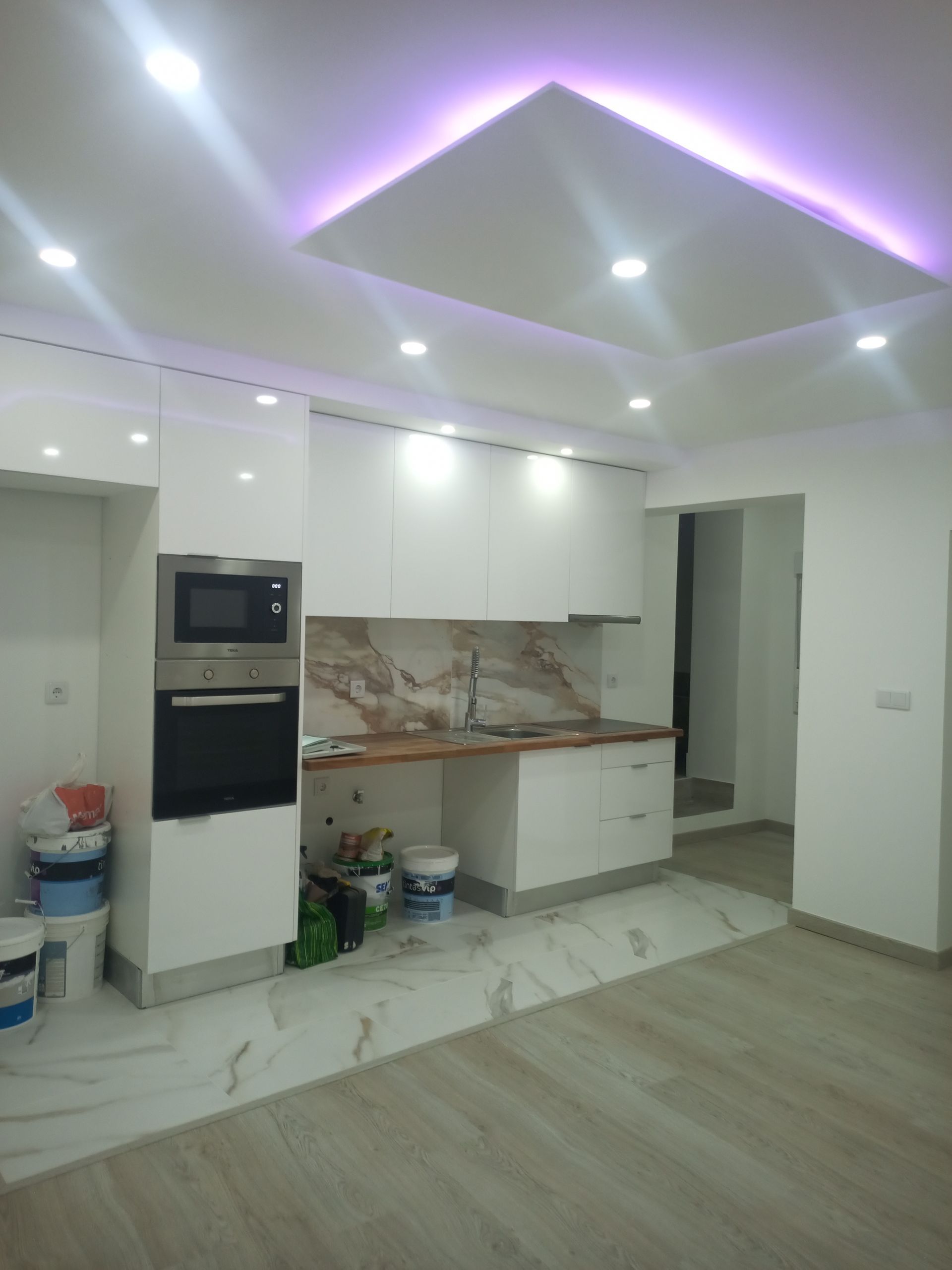 Cozinha moderna branca com eletrodomésticos embutidos, iluminação embutida e backsplash de mármore.